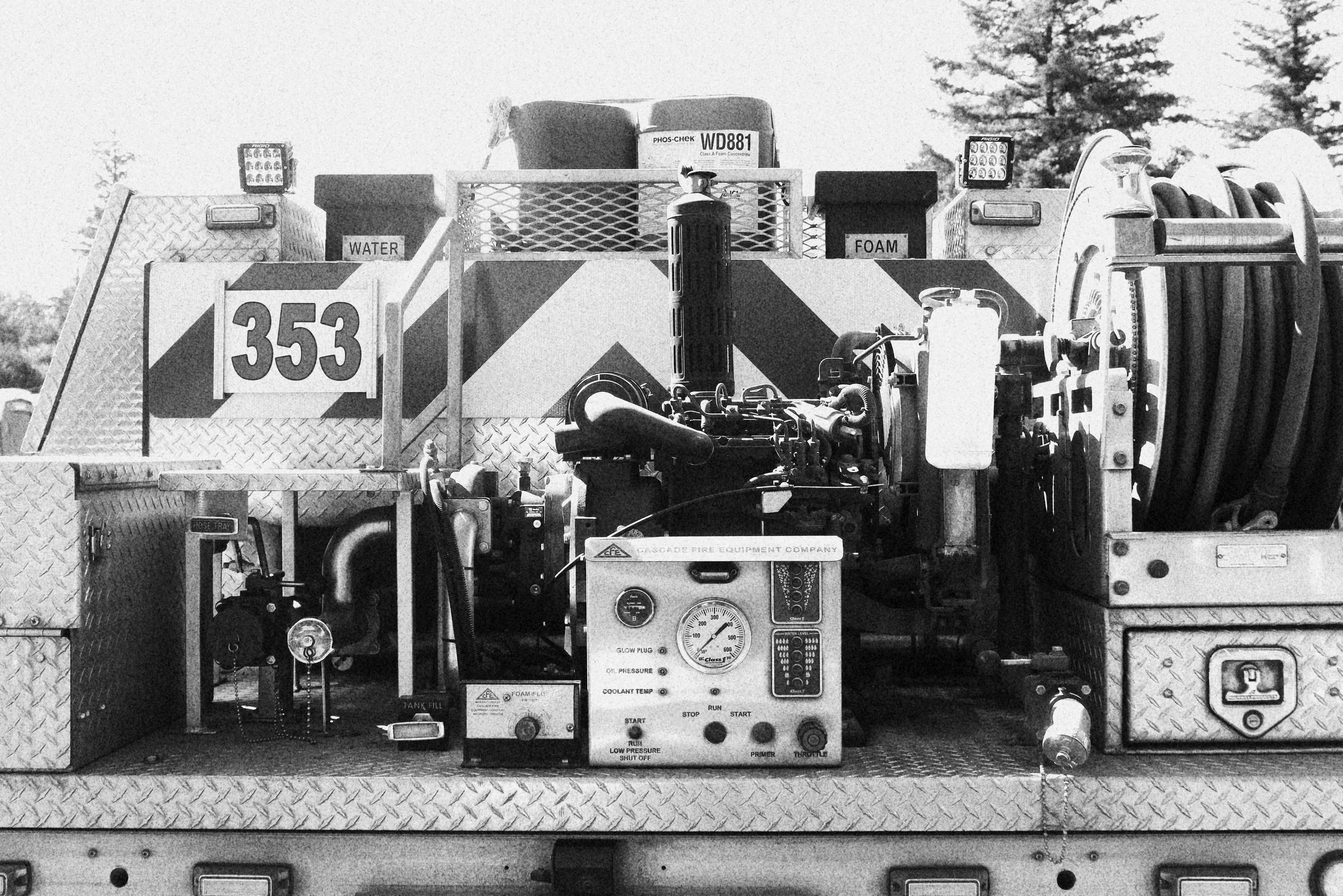 Black and white photo of a fire truck with equipment and hoses, labeled with '353', and signs indicating 'Water' and 'Foam' on top.