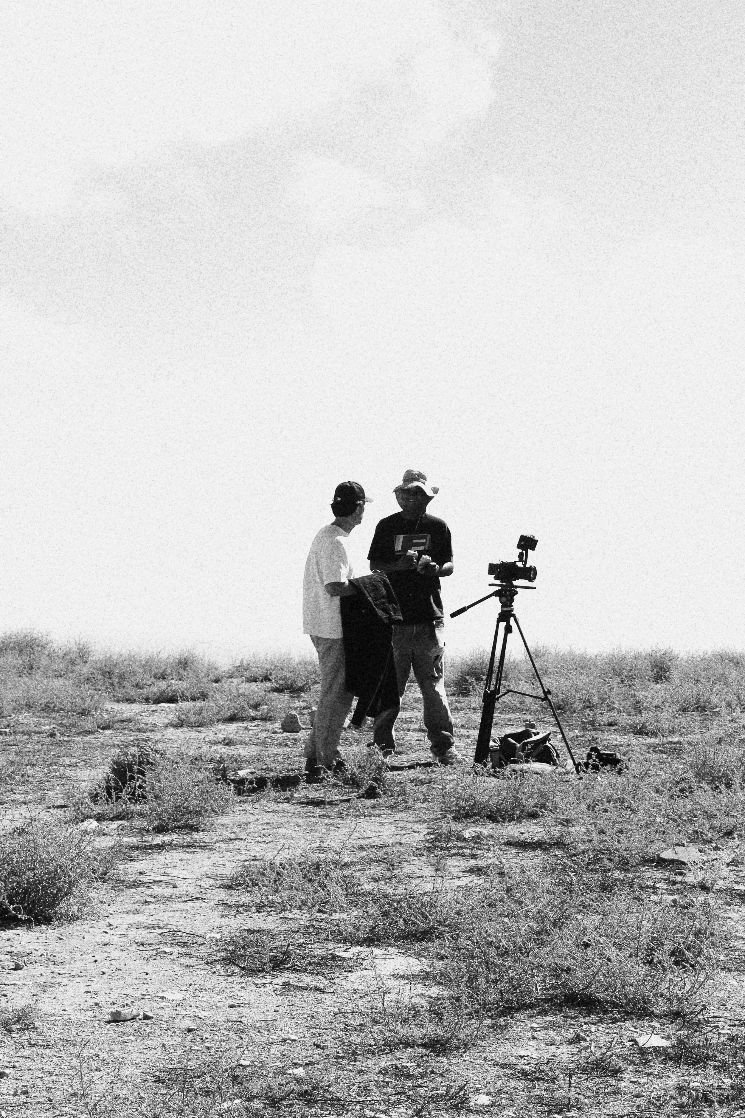 Two people setting up filming equipment in a barren desert landscape