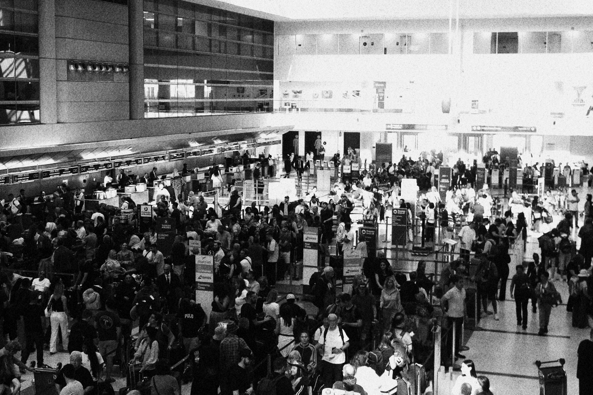 Crowded airport terminal with many travelers in line at check-in counters and security screening area.