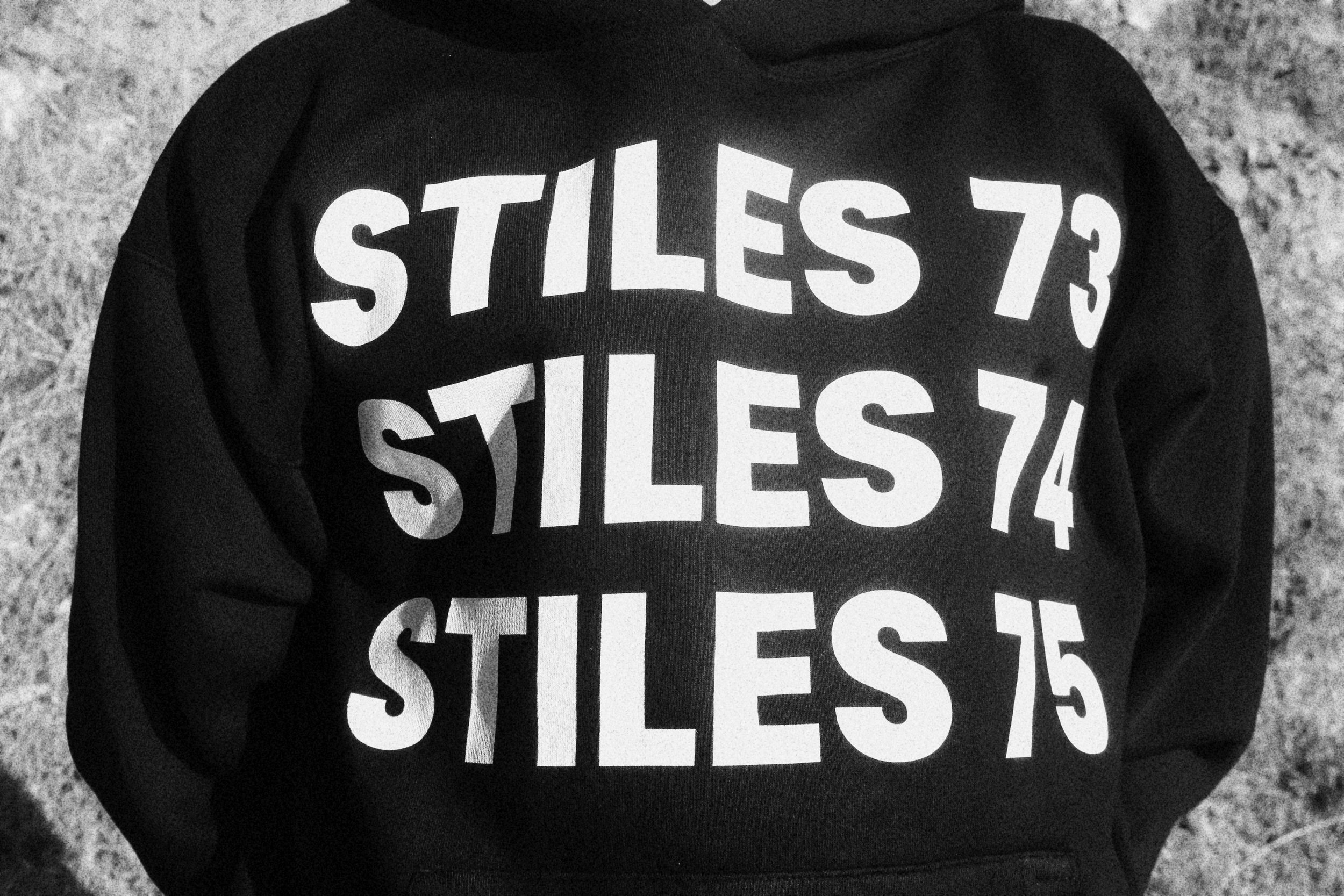Close-up of a black hoodie with white text that reads "STILES 73" repeated three times on the front.