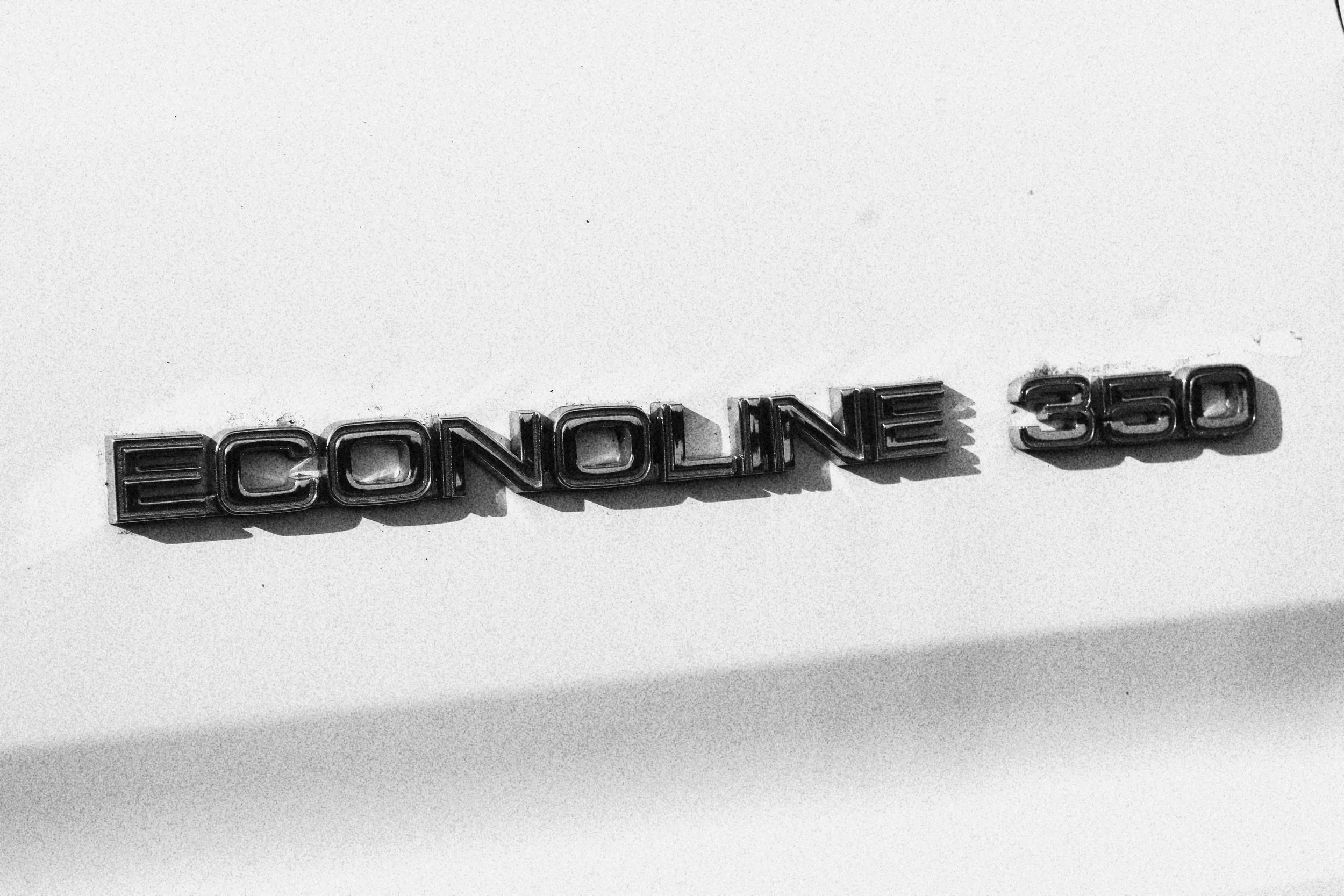 Close-up of an 'ECONOLINE 350' emblem on a vehicle's exterior in black and white.