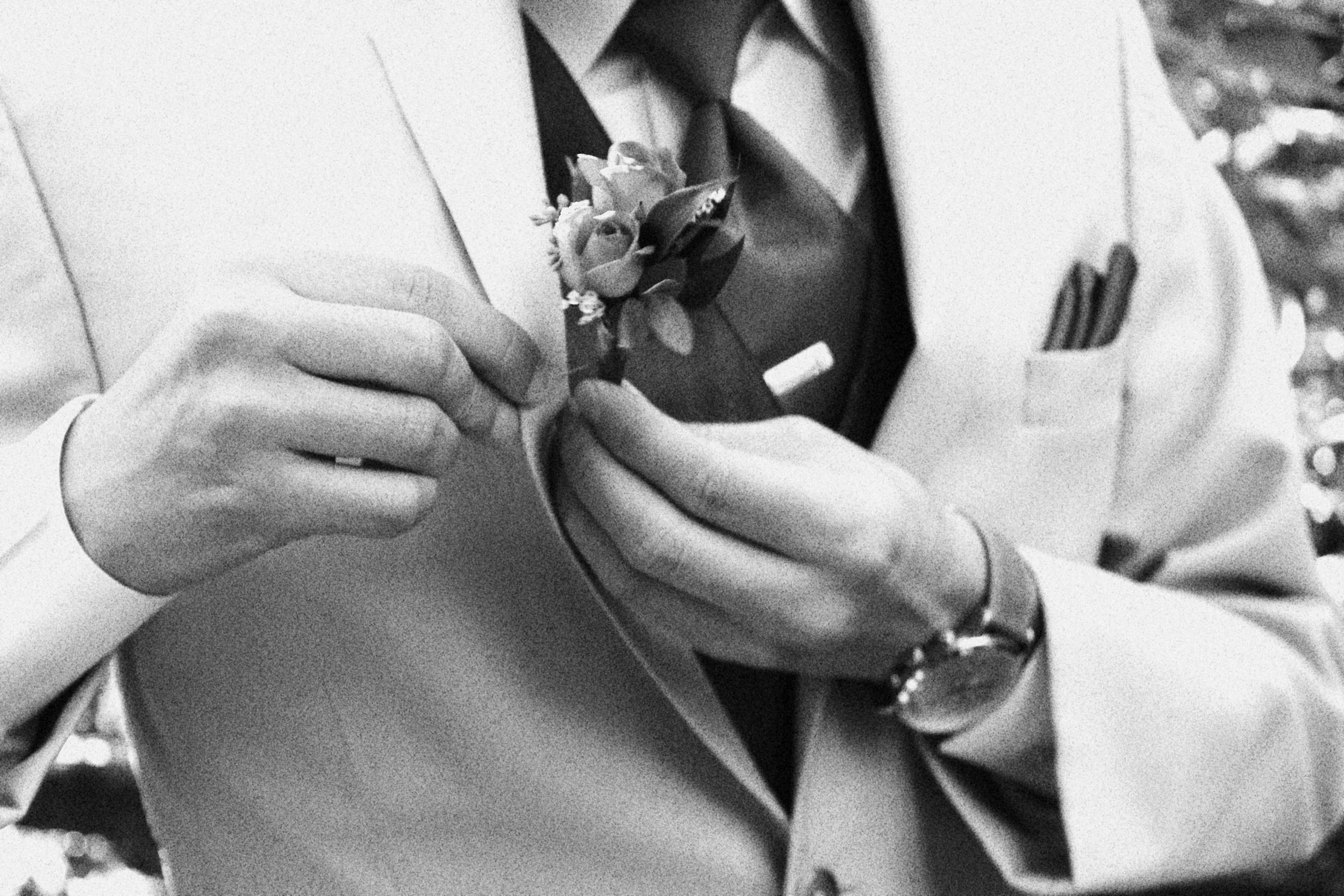Man in a suit and tie adjusting a boutonniere on his lapel.