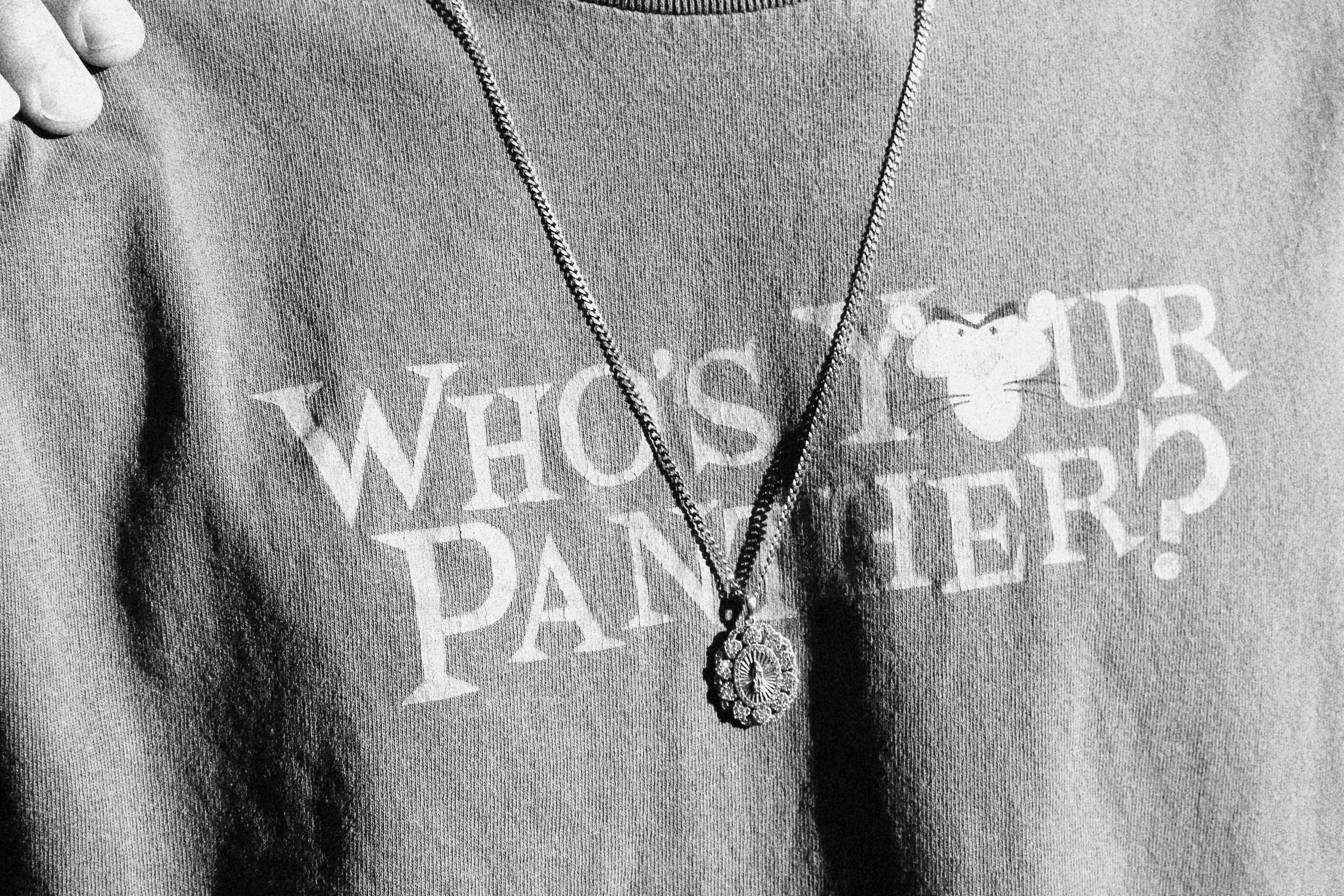 Close-up of a person wearing a sweatshirt with the text 'Who’s Your Daddy?' and a chain with a pendant necklace featuring a decorative oval design.
