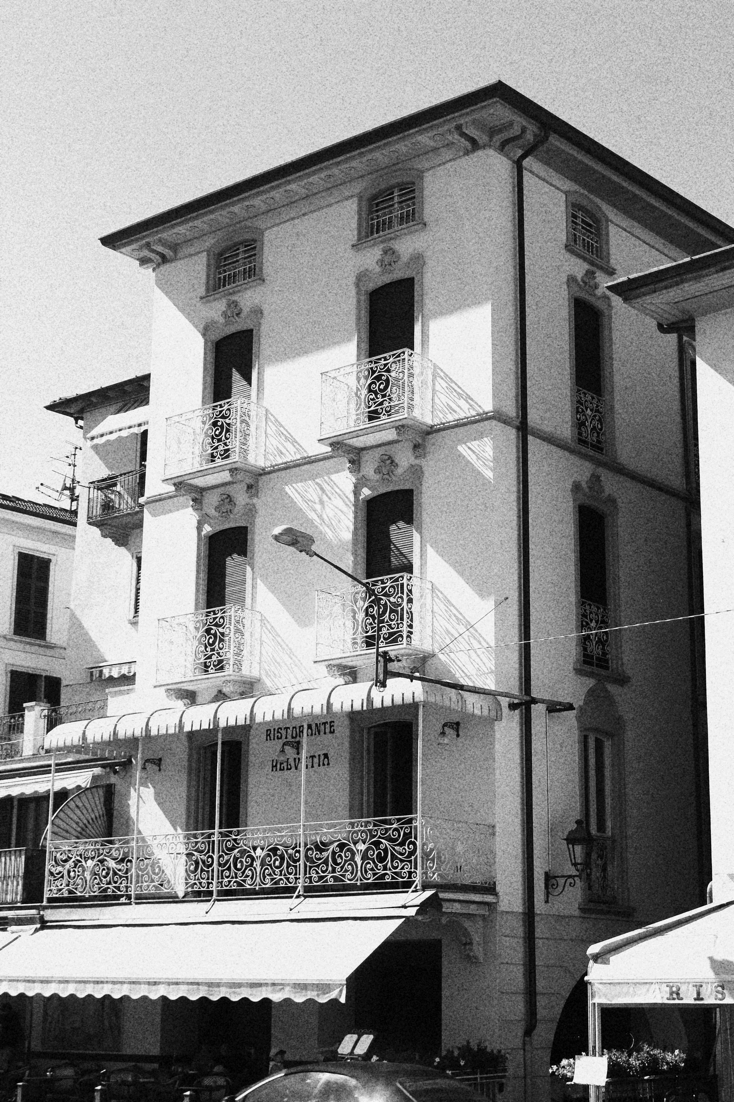 Black and white photo of a multi-story building with balconies and ornate iron railings, and a restaurant on the ground floor with a sign that reads 'Ristorante'