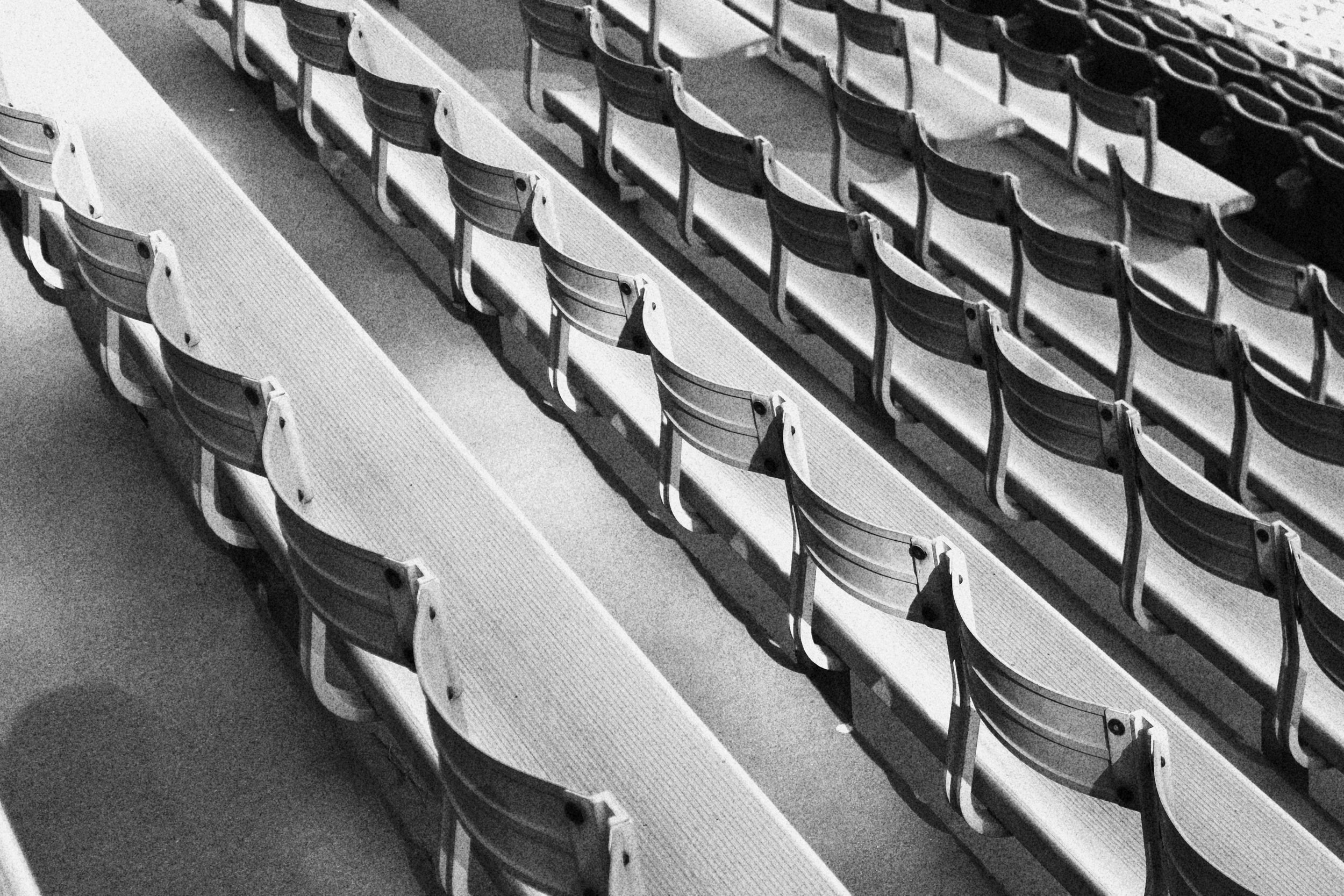 Empty stadium seats in monochrome, arranged in rows with shadows cast on the seats and floor.