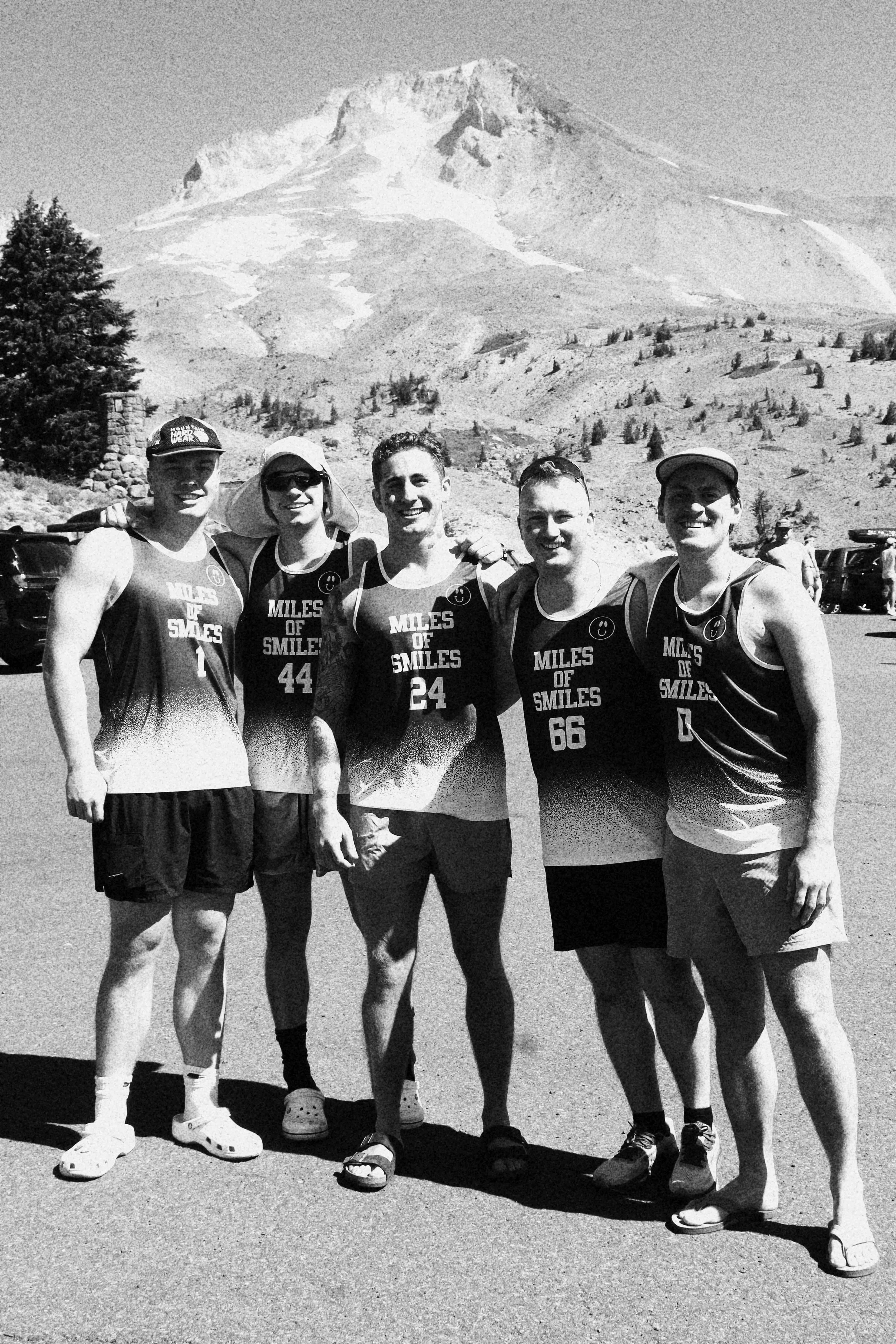 Group of five young men in athletic gear standing together outdoors with mountain in the background.