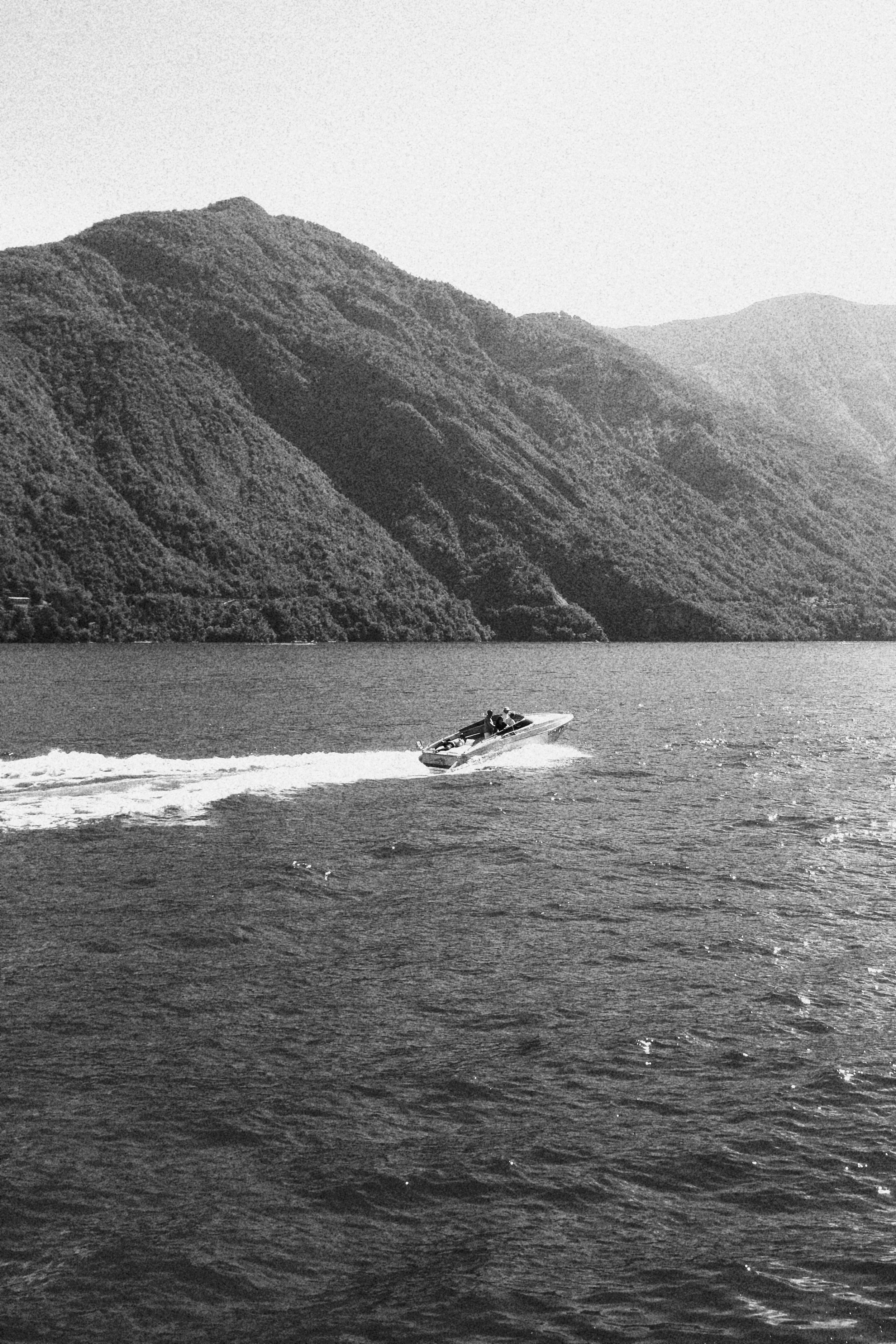 A speedboat racing across a body of water with mountains in the background in black and white