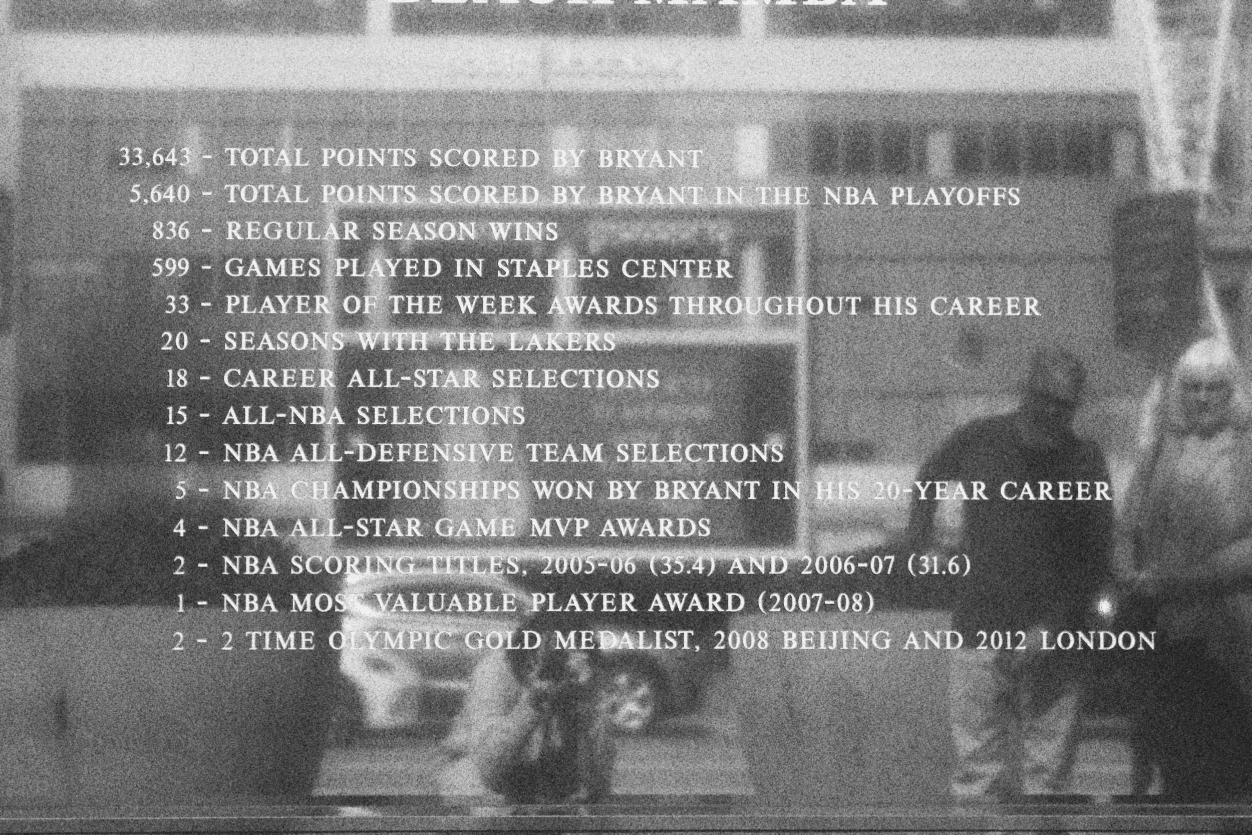 List of statistics and achievements related to Bryant, including total points scored, NBA playoff points, seasons with Lakers, awards, and medals, displayed over a blurred background of a basketball court and people.