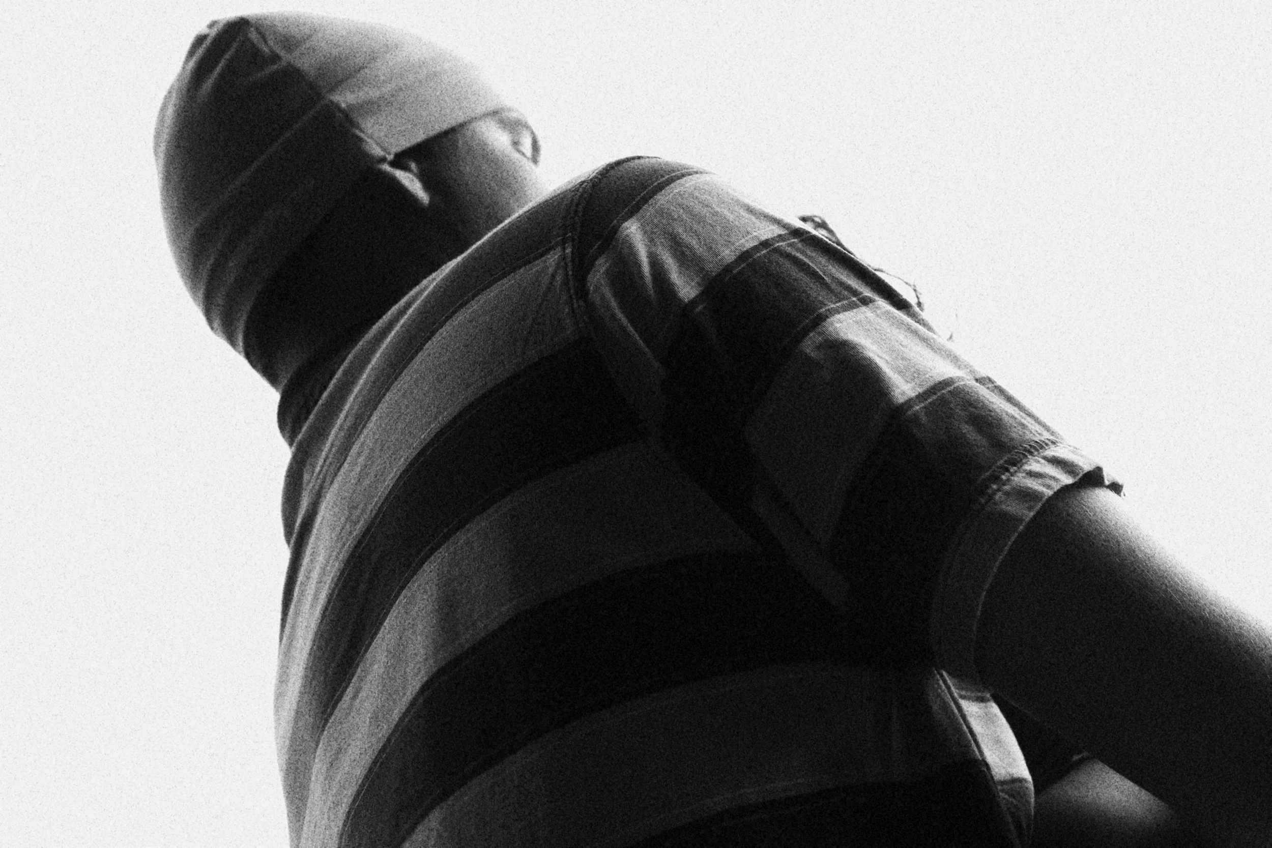 A person wearing a striped shirt and a cap, viewed from a low angle against a bright sky.