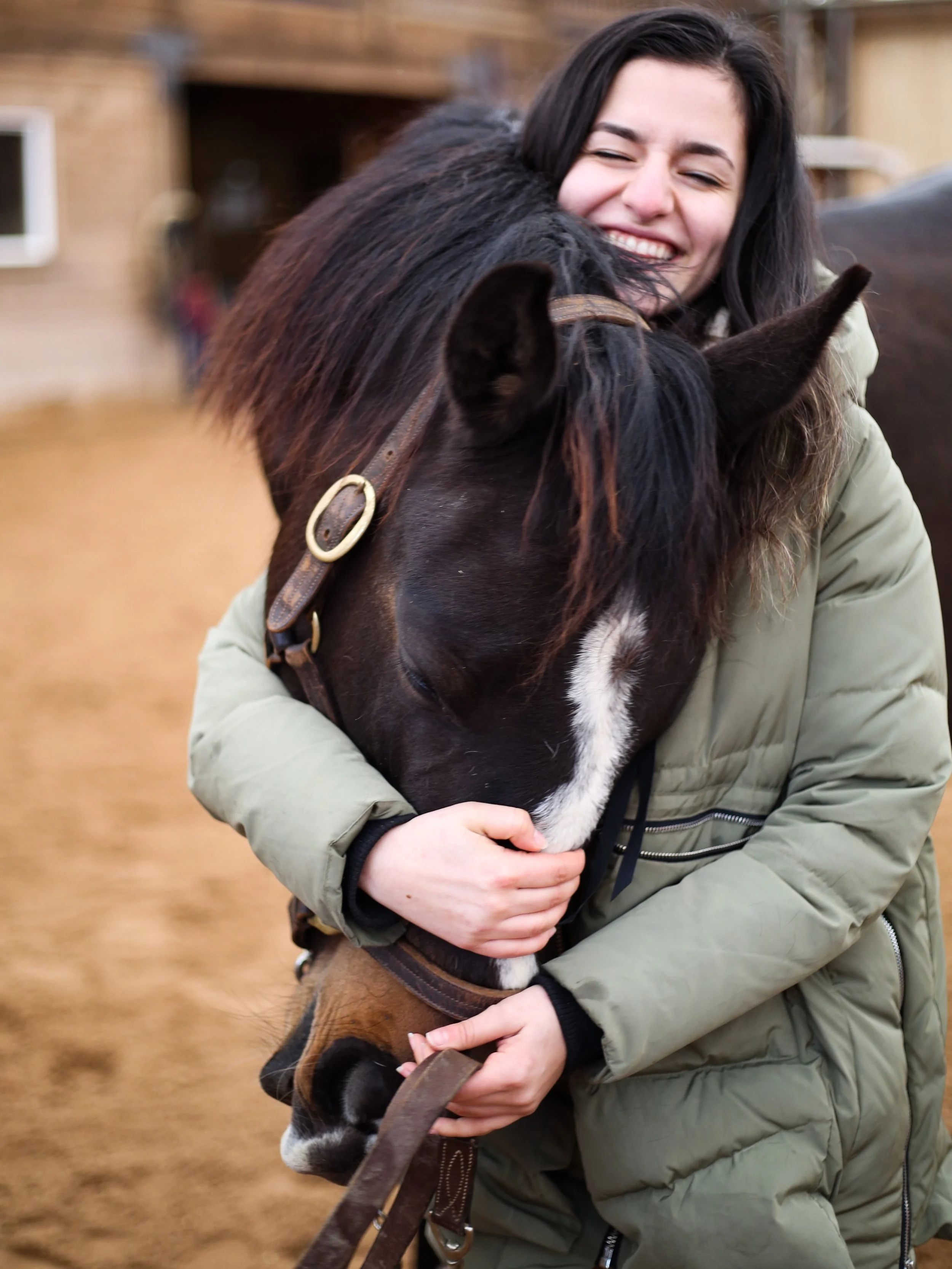 A woman hugging a black horse with a white stripe on its face at a stable.