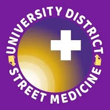 Logo for University District Street Medicine, featuring a purple background, a white plus sign, and a yellow circular gradient with white text encircling it.