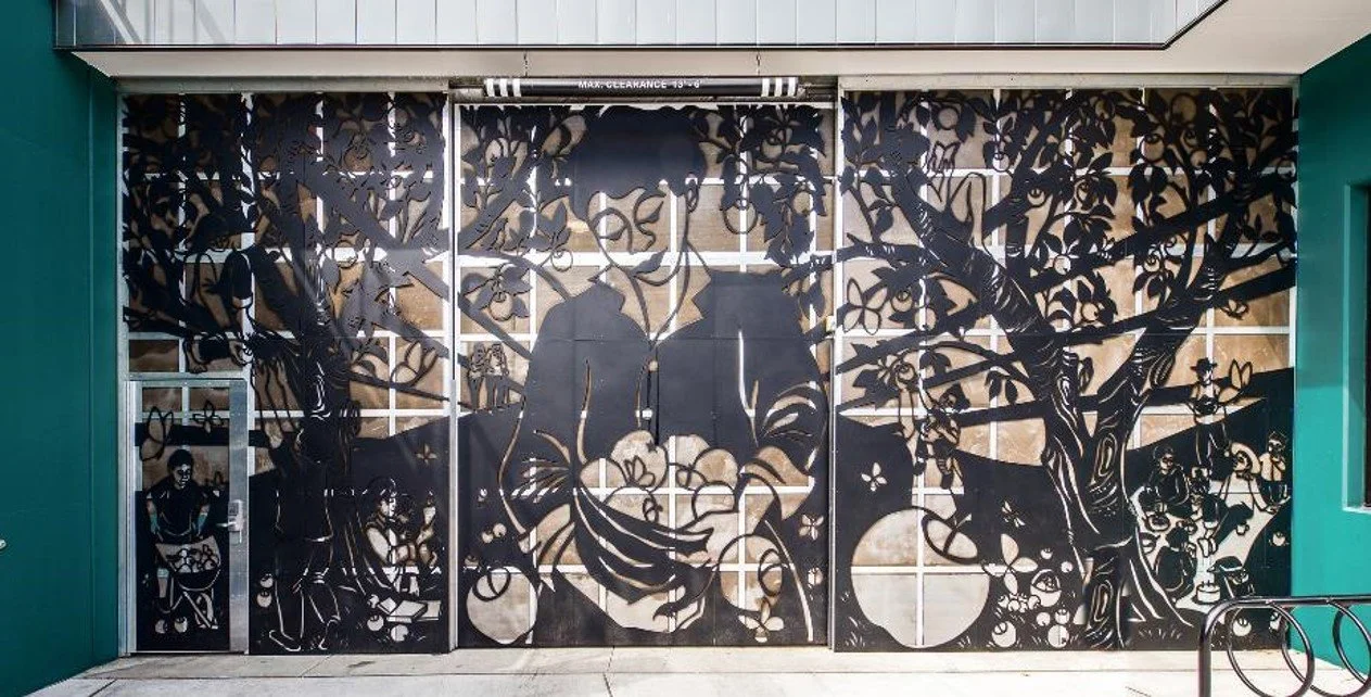 Metal gate mural depicting people working under a tree, with a man and woman in the center