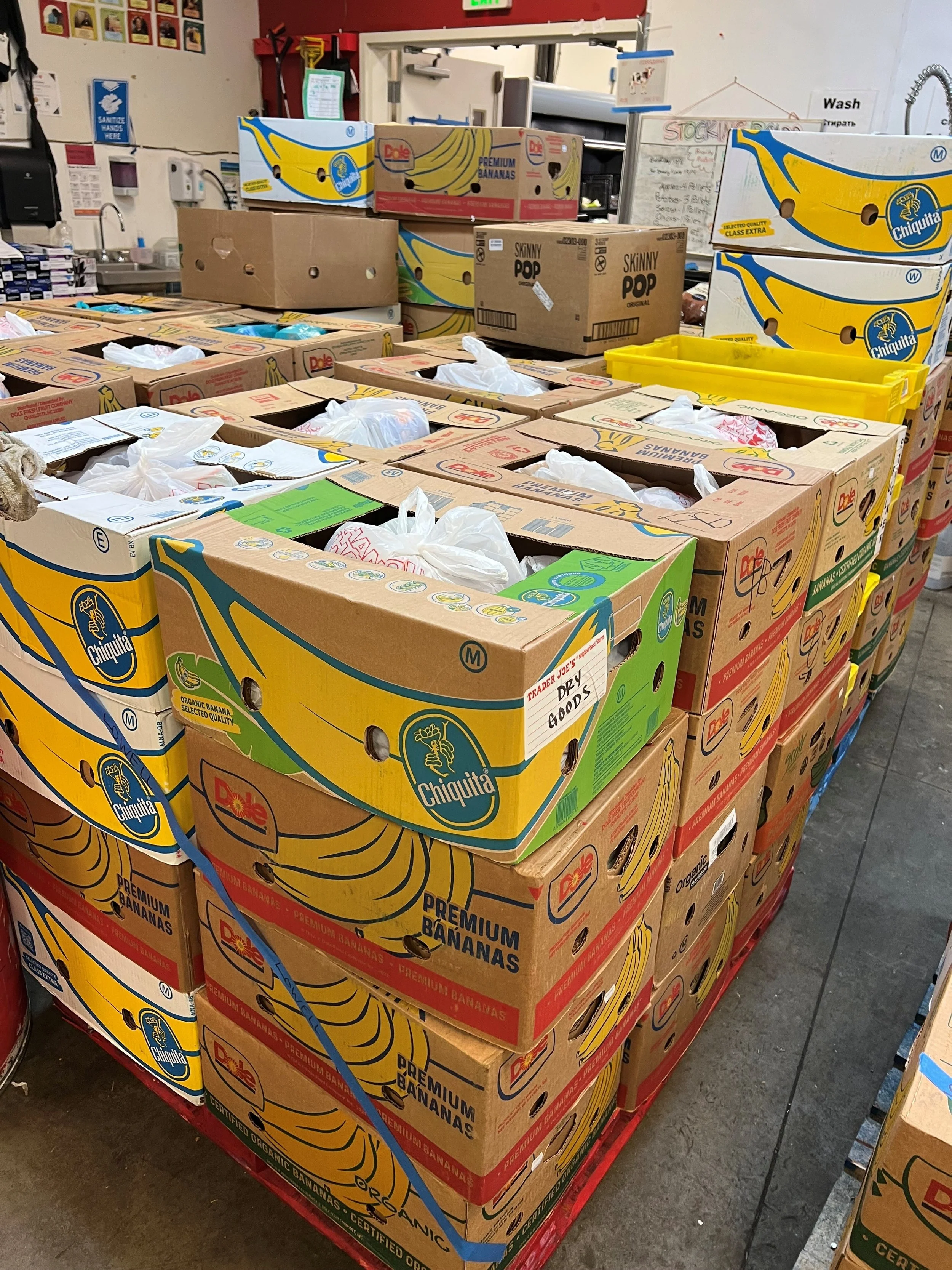 Stacked boxes of Chiquita bananas in a grocery store aisle, with some boxes labeled 'Premium Bananas' and 'Organic Bananas'.