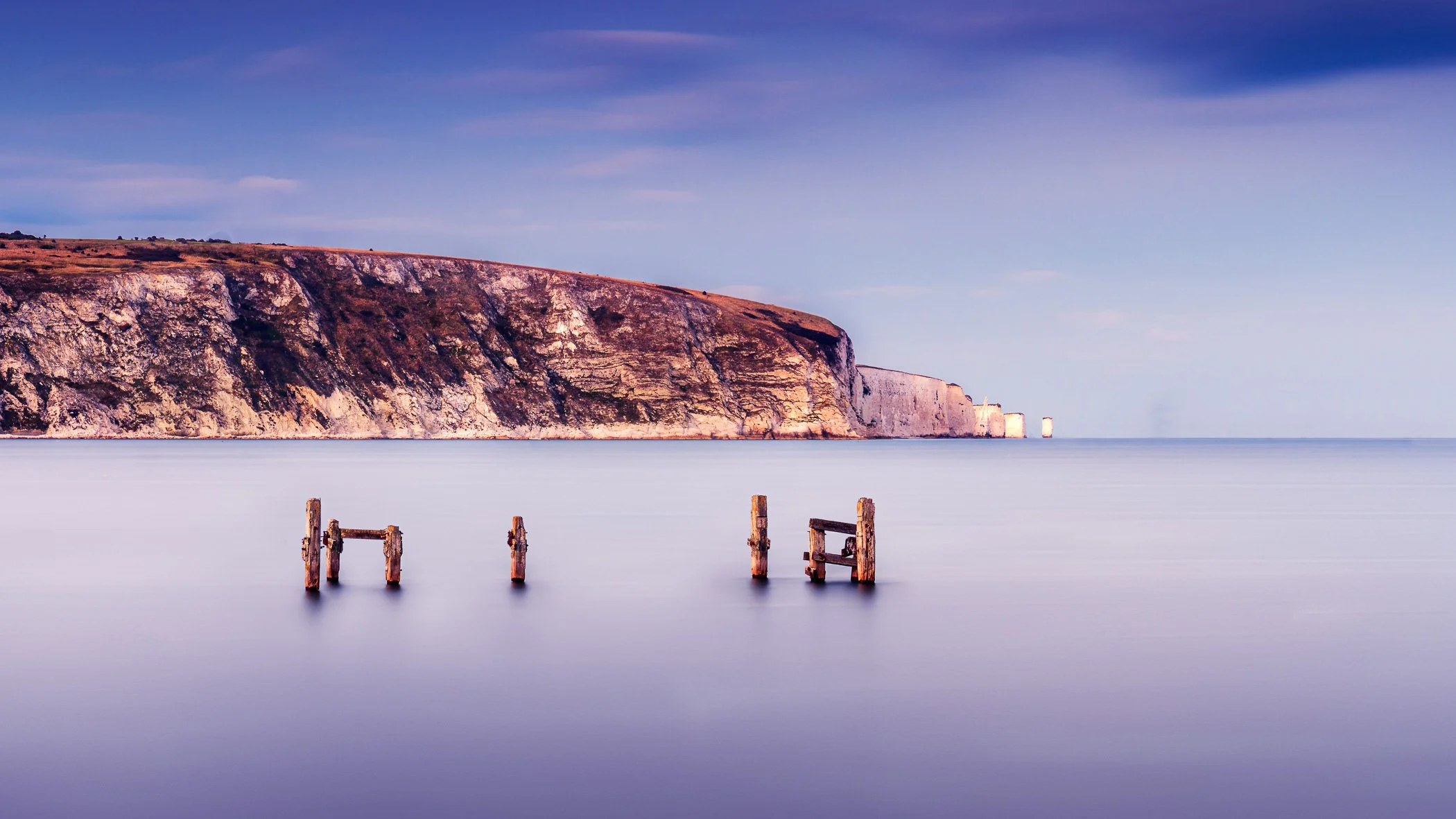 Quiet Remains A minimalist composition depicting historic wooden pilings silhouetted against soft, diffused coastal light.
