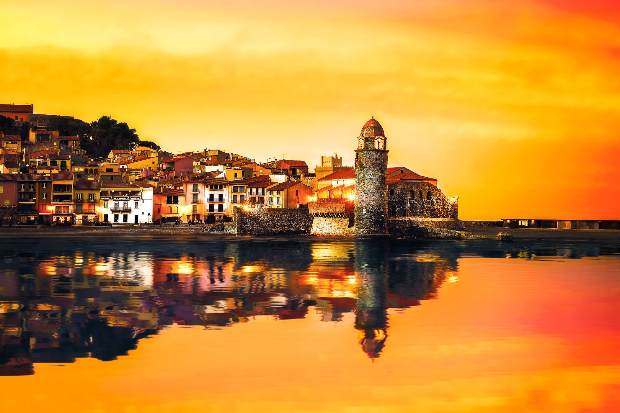 Sunset Glow over Collioure Harbour A dramatic sunset composition featuring rich warm hues illuminating the harbor waters and surrounding hills.