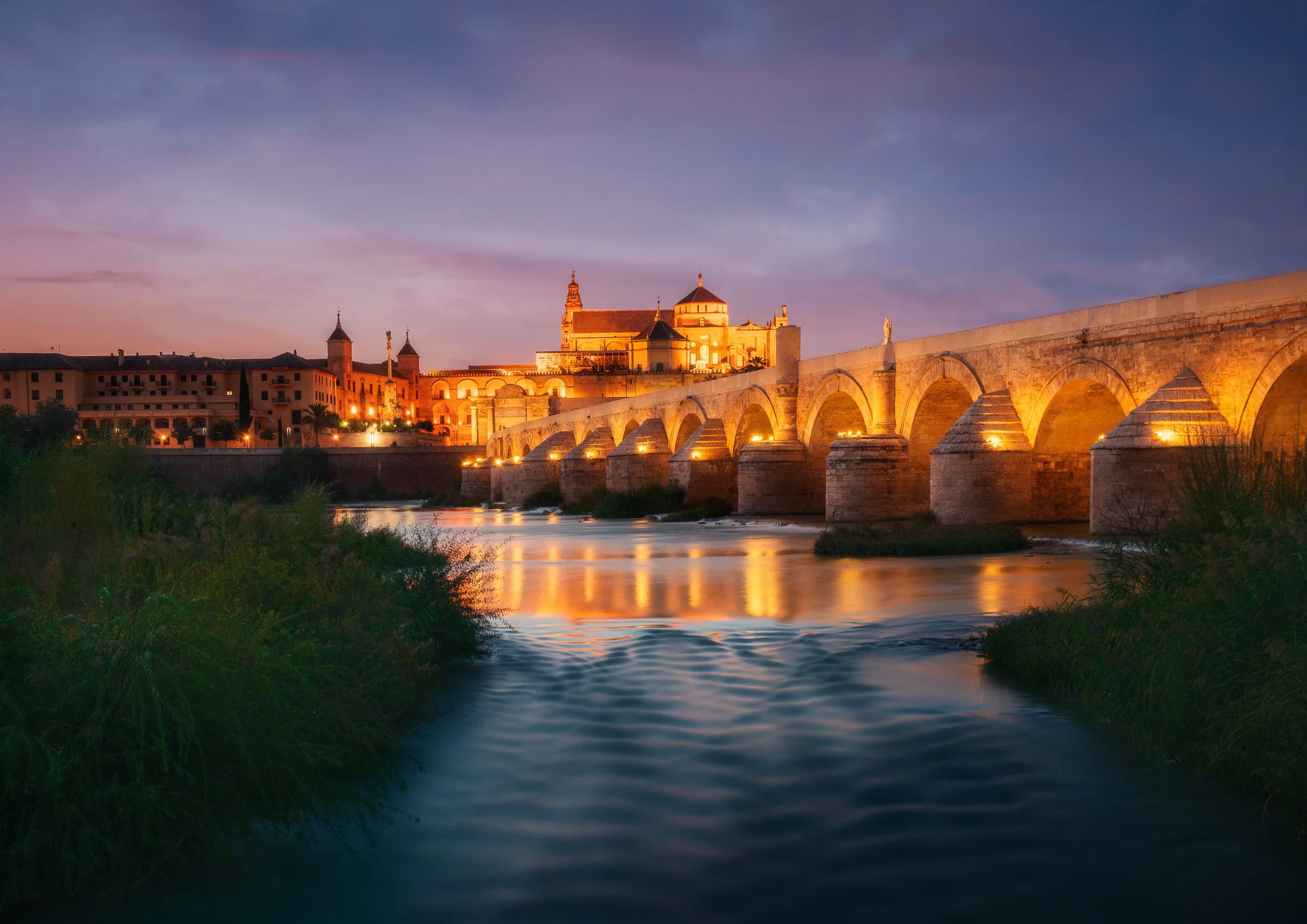 Twilight Over Cordoba A serene view of the city skyline and historic architecture reflecting across the river at dusk.