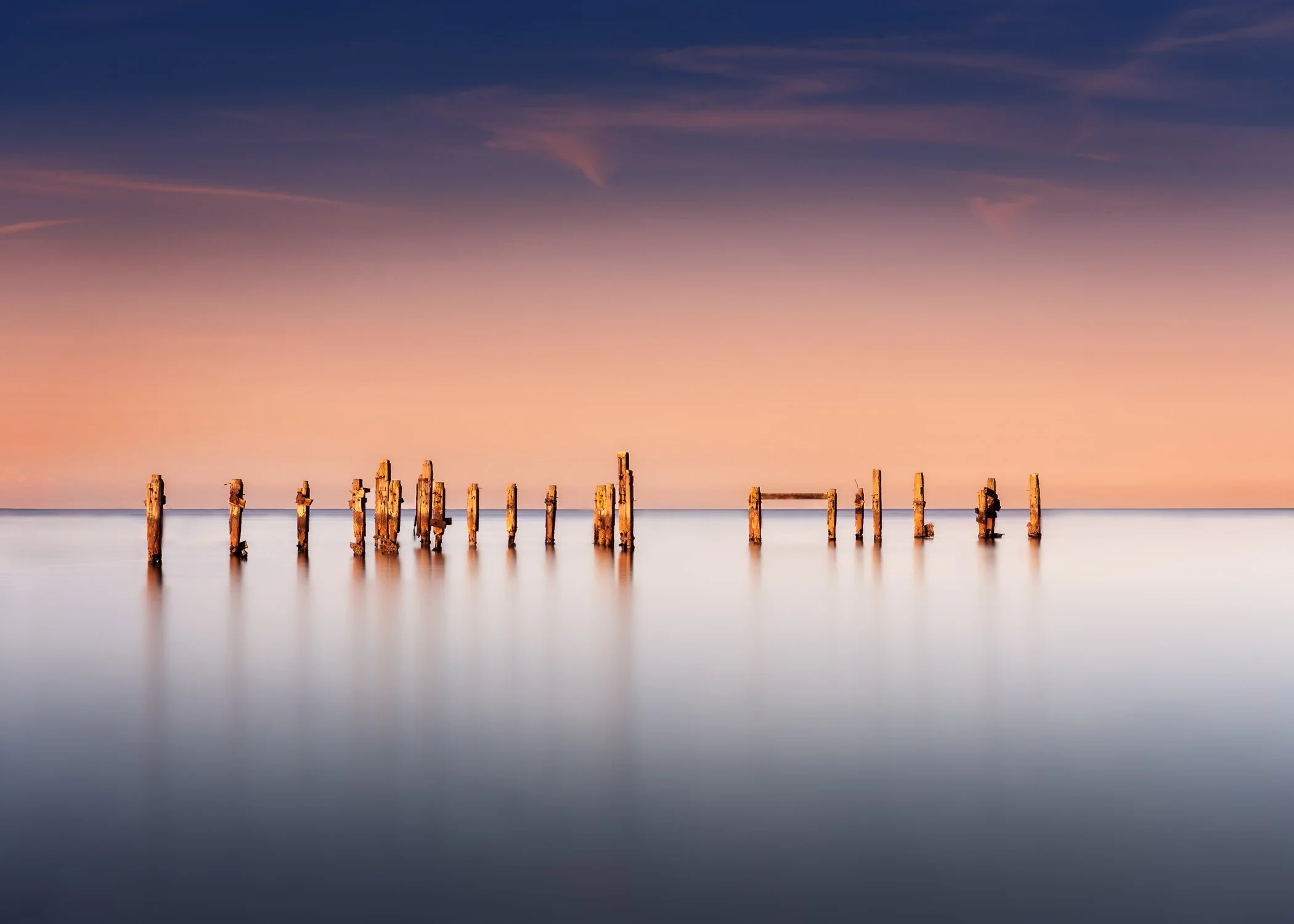 Weathered wooden posts standing in the calm water of Swanage Bay beneath a soft sky