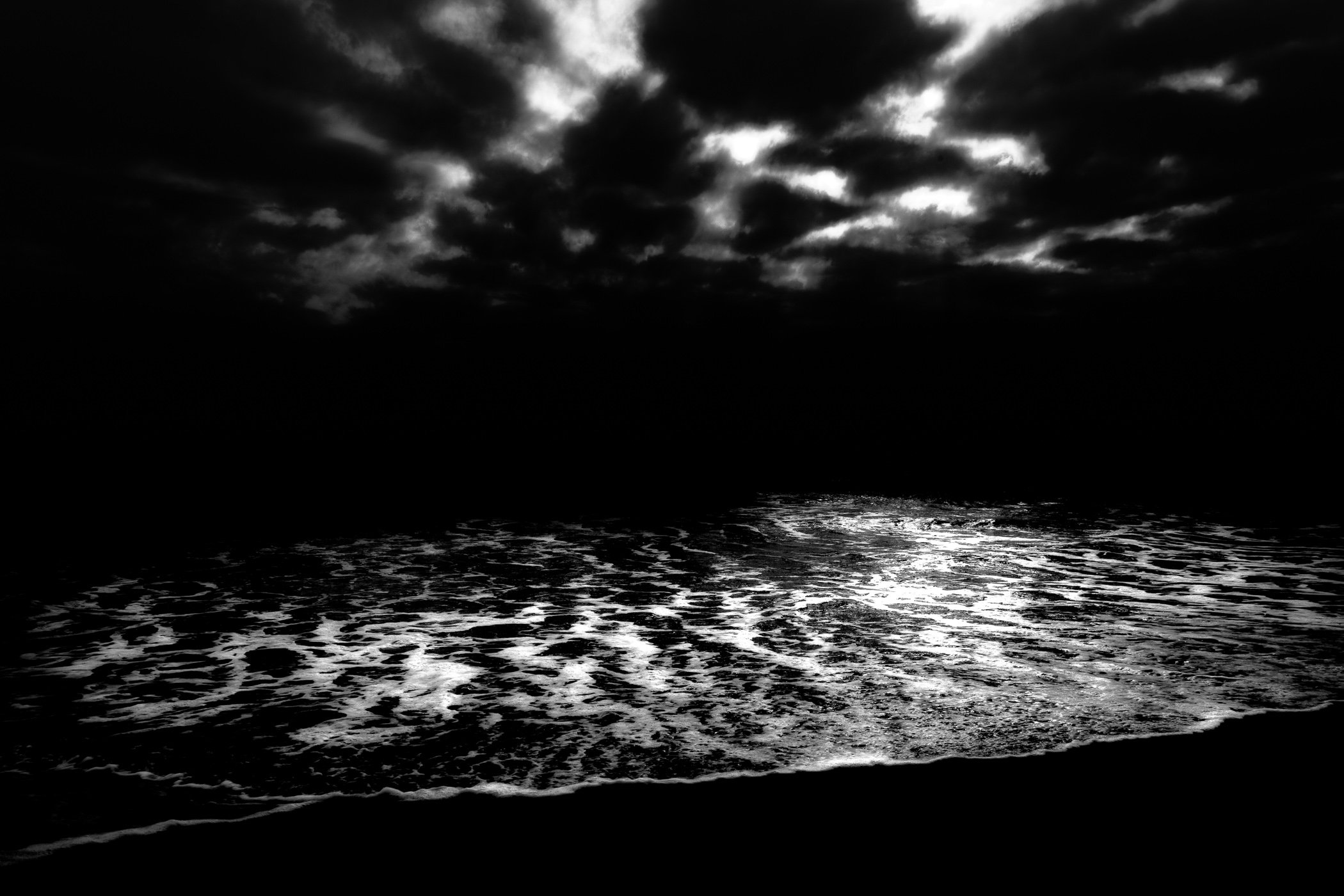 Whispers of Light A dramatic monochrome capture of moonlight shimmering across breaking ocean waves under a tempestuous sky.
