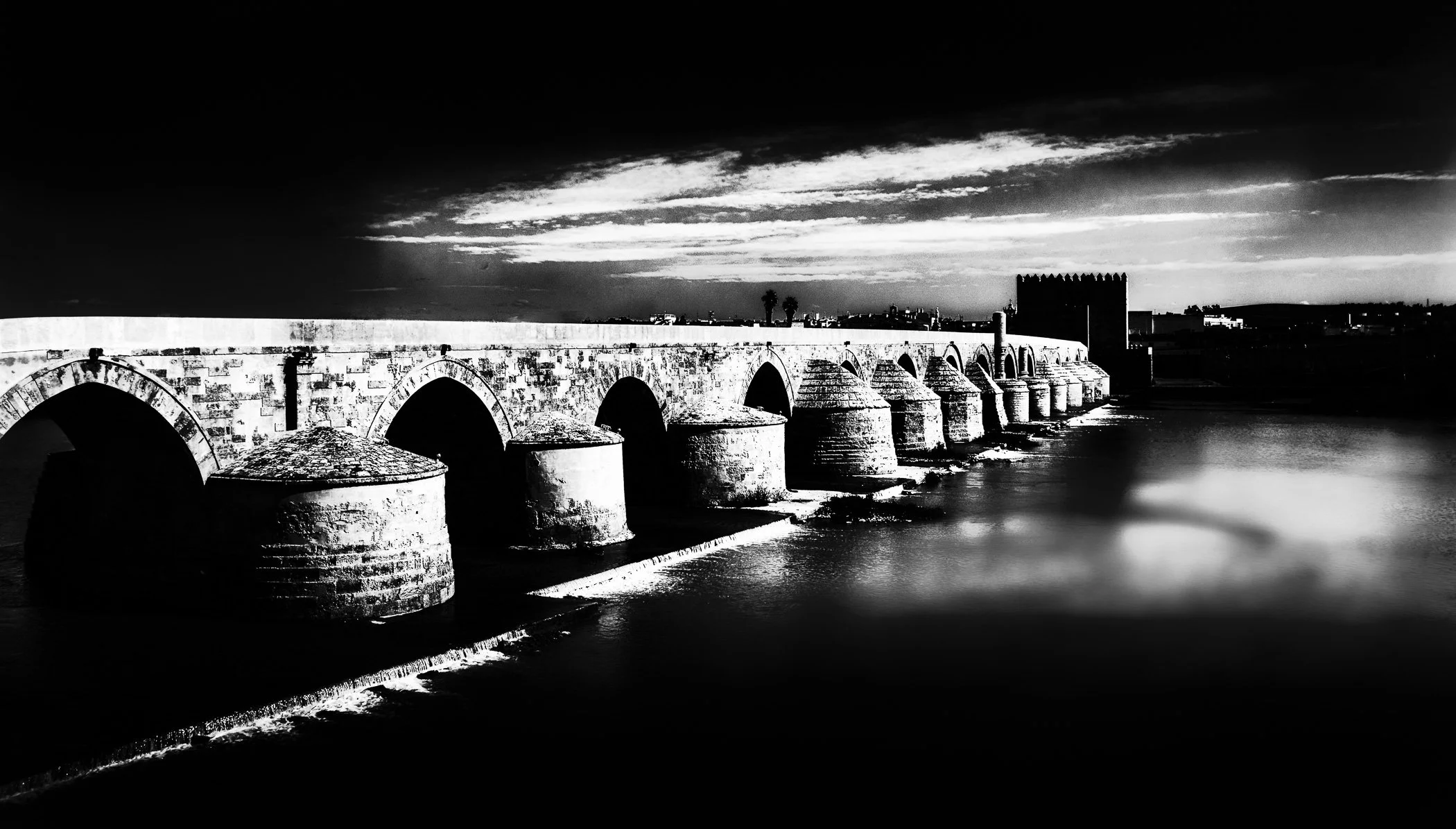 The Roman Bridge of Cordoba A striking black and white perspective highlighting the timeless stone arches spanning the Guadalquivir.