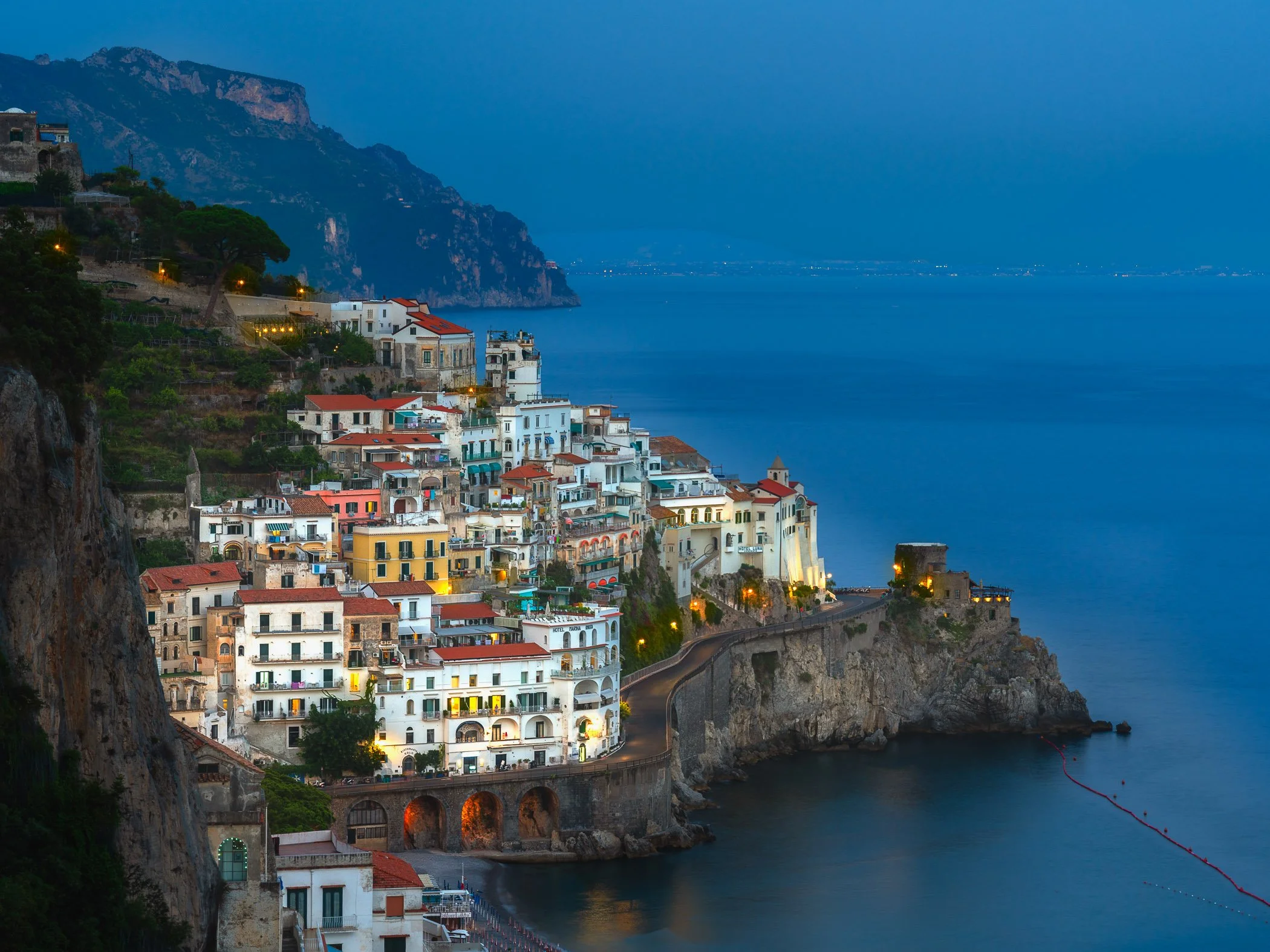 Amalfi at Blue Hour A serene twilight photograph capturing the cliffside town of Amalfi as streetlights begin to glow against the cool evening sky.