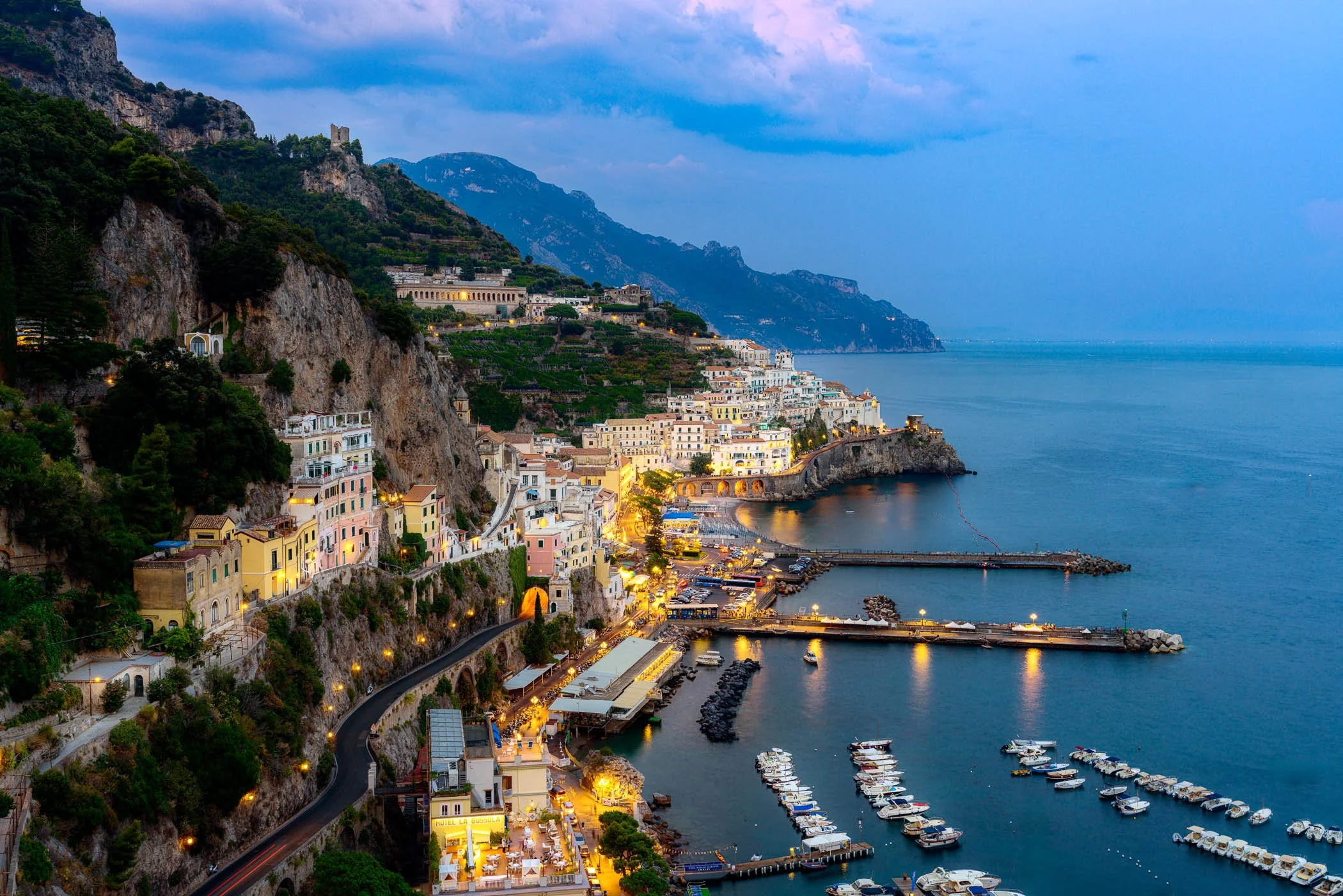 Twilight Tranquility at Amalfi An atmospheric evening scene highlighting the quiet beauty of the coastline and glowing lights reflected across calm waters.