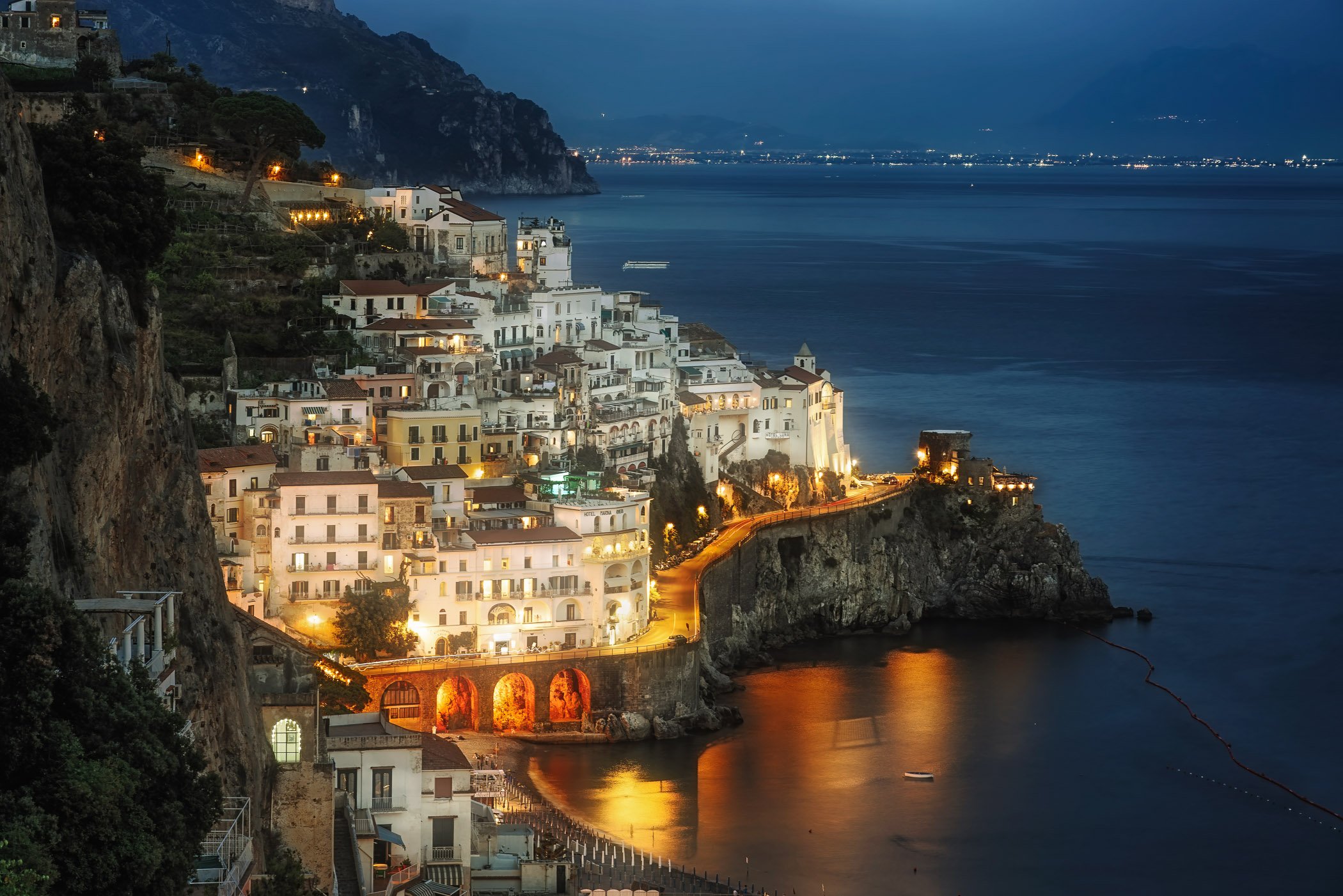 Amalfi Town Illuminated A vibrant night photograph showcasing the warm, glowing lights of Amalfi nestled between the towering rock faces and the dark sea.