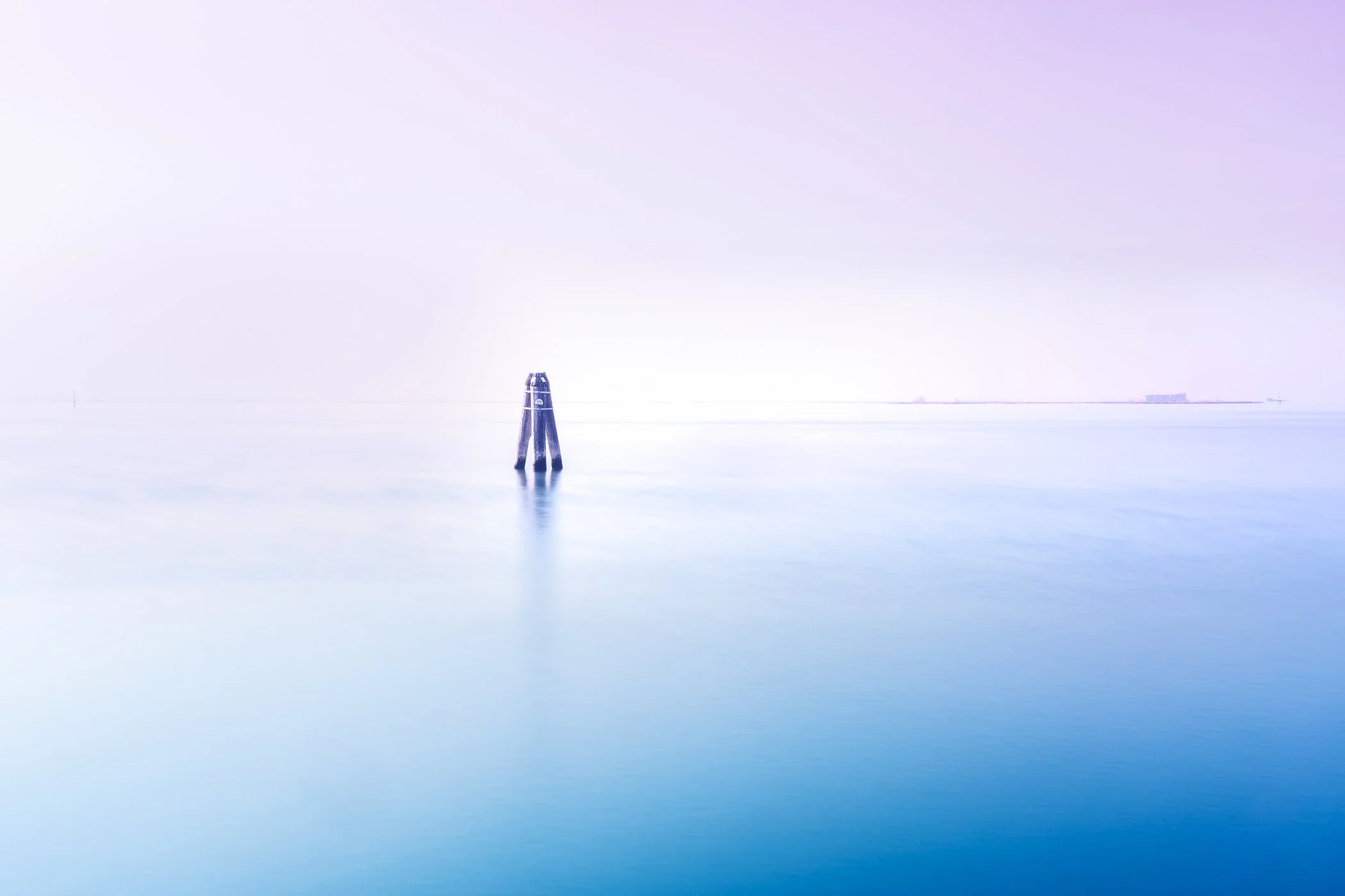 Marker in Still Water A serene, minimalist long exposure shot featuring a solitary wooden mooring post standing in calm, glassy waters.