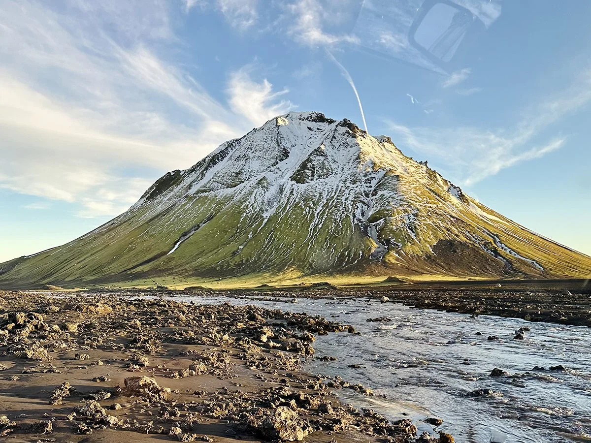 Snow-dusted volcanic mountain rising above a river and lava fields in Iceland