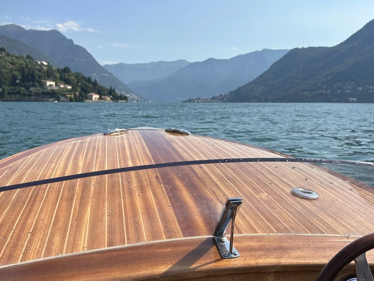 View from a wooden boat traveling across Lake Como toward mountain villages