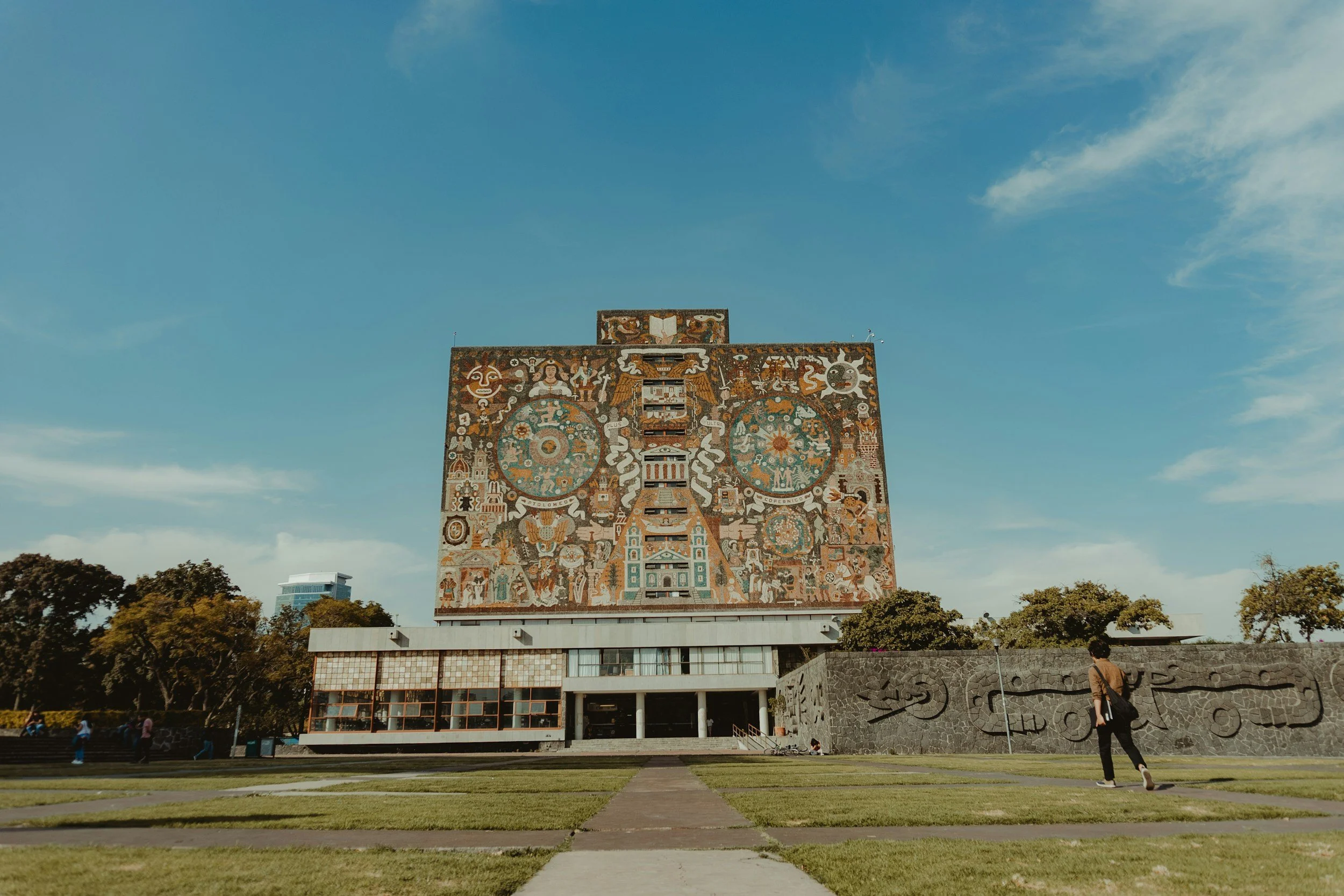 Edificio con mural colorido en una ciudad, con personas caminando en el parque