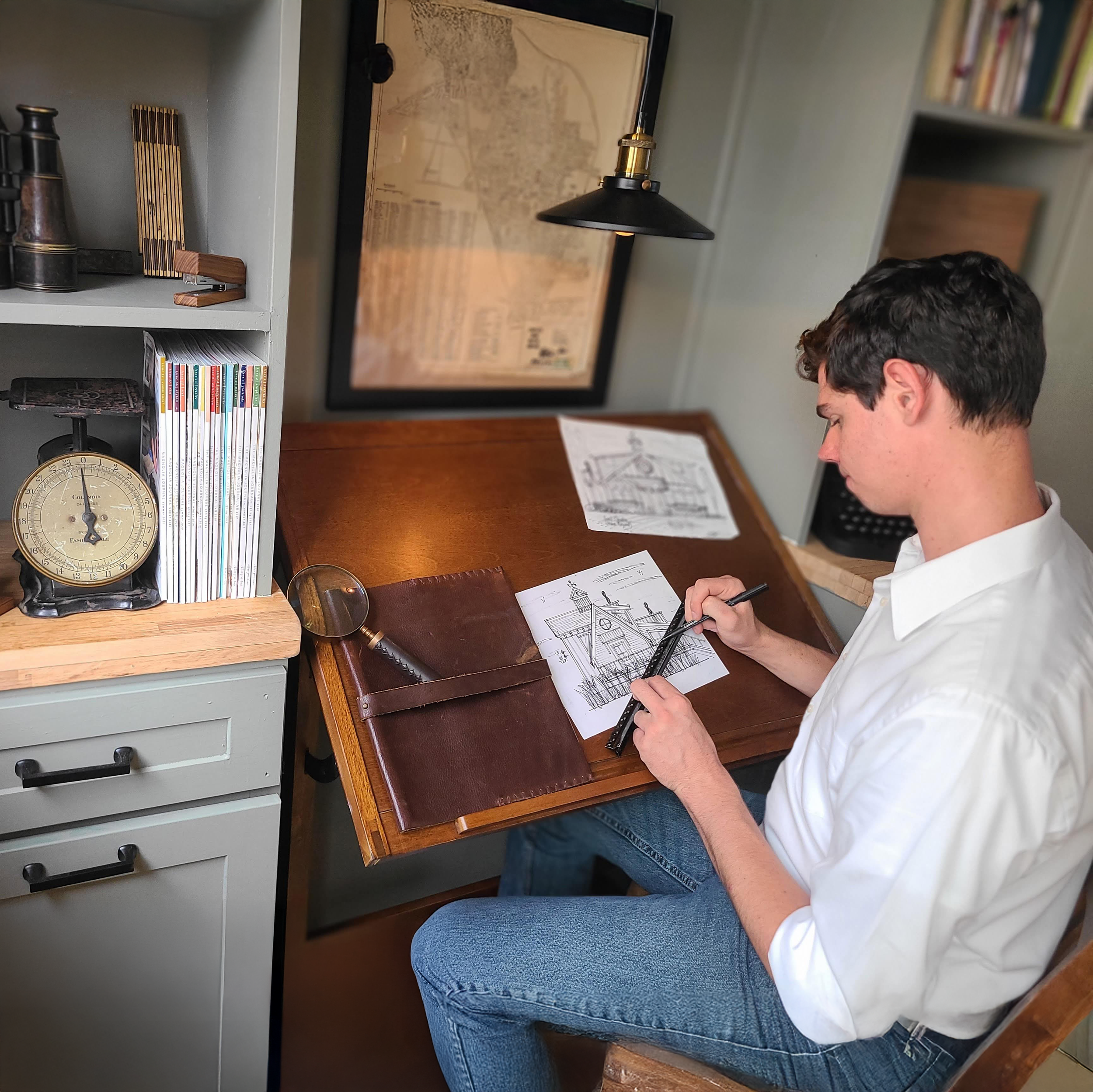 Architect Brian Johnson sketching custom home design plans at drafting desk in Levittown, NY – Americana Architects.