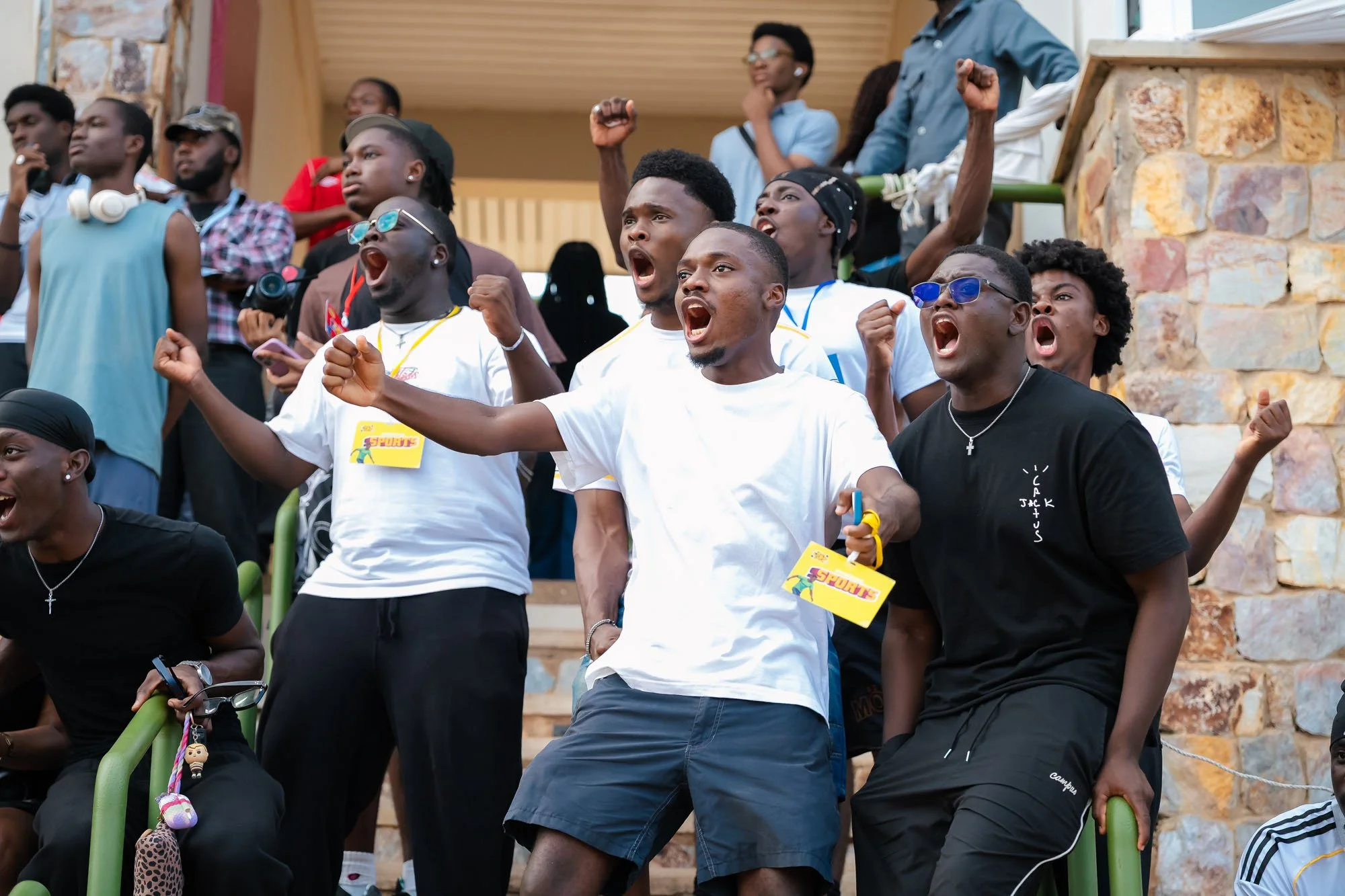 Group of young people cheering and shouting, some with fists raised, at an outdoor event.