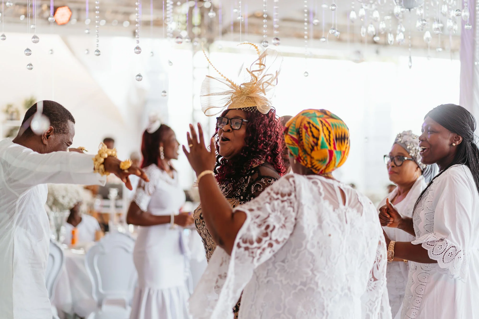 Group of people at a celebration, dancing and smiling in a well-lit venue decorated with crystal ornaments.