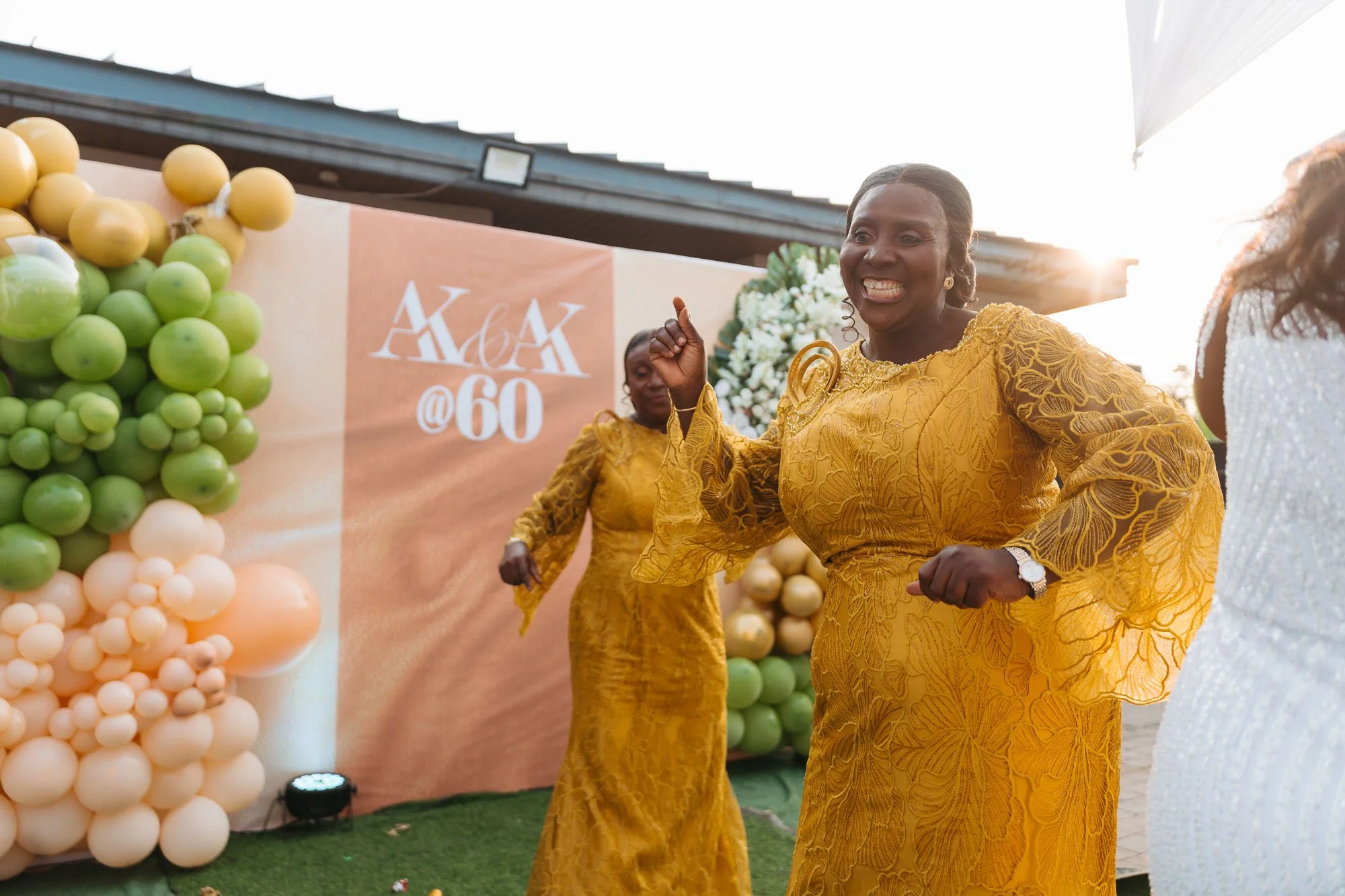 Women dancing outdoors, celebrating a 60th birthday, with a backdrop decorated with balloons and flowers.