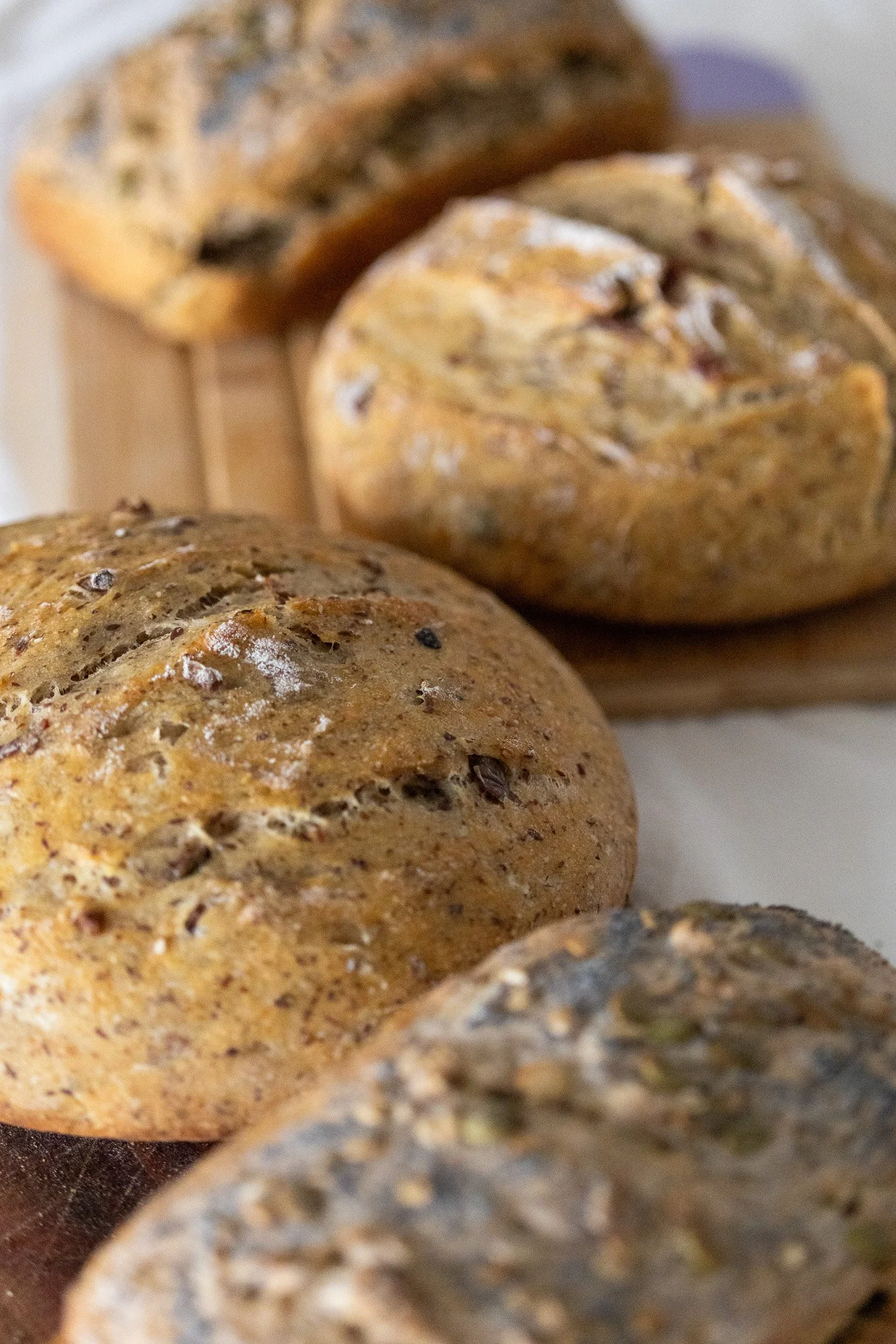 Close-up of assorted baked Arctic Sourdough bread loaves with seeds and herbs topping, arranged on a wooden surface.