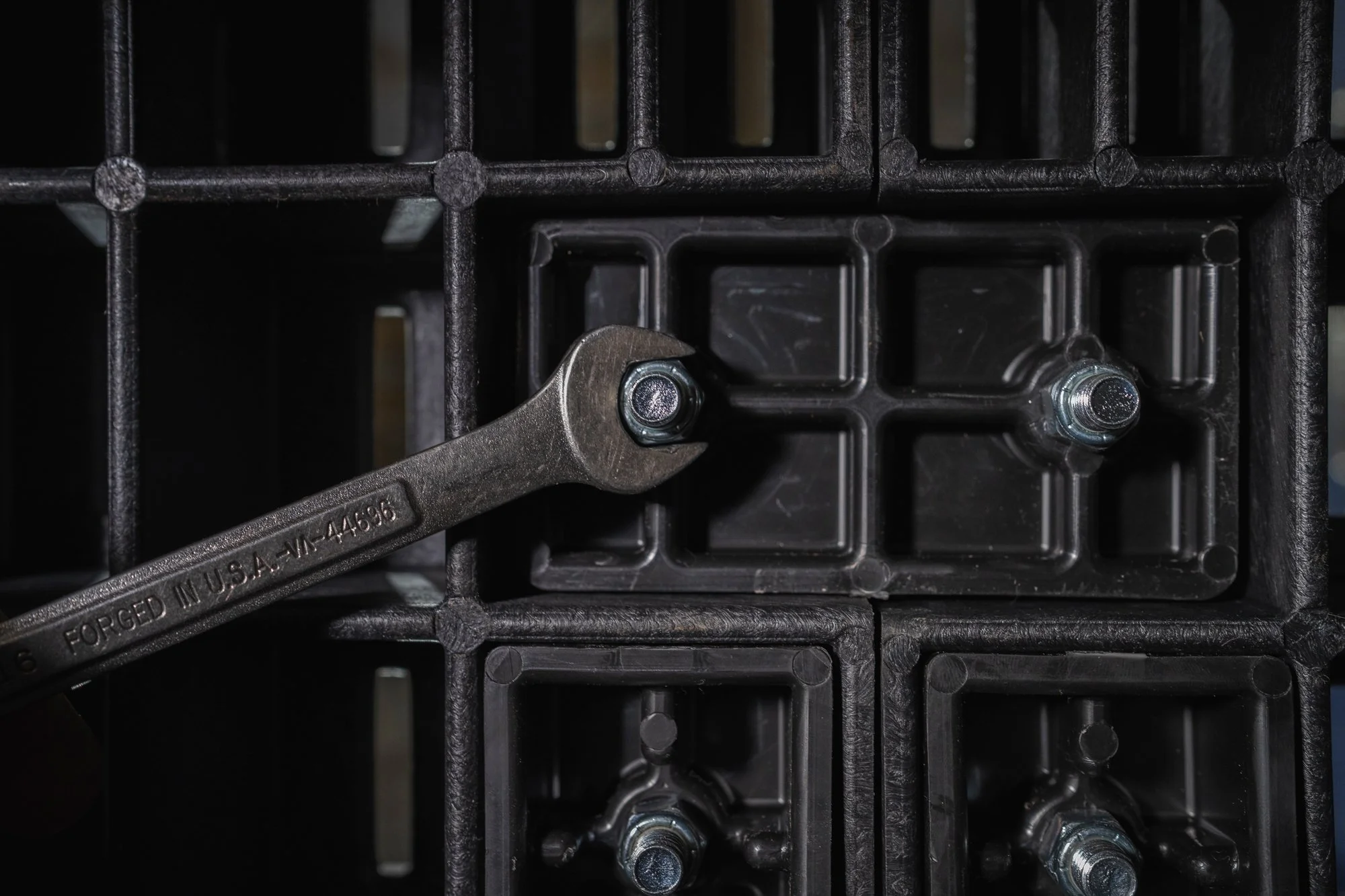Close-up of a wrench tightening a bolt on a plastic grid frame with metal bolts.