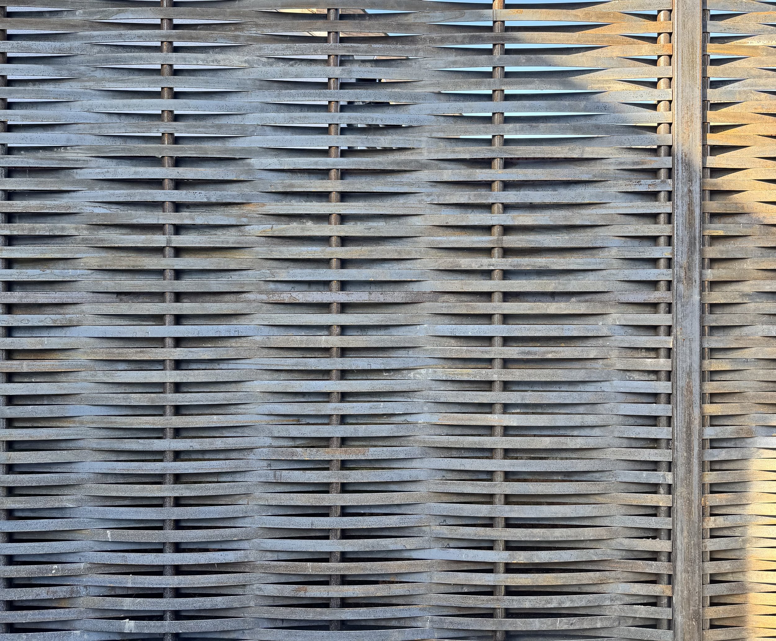 A close-up view of a weathered wooden lattice fence with horizontal slats and vertical supports.
