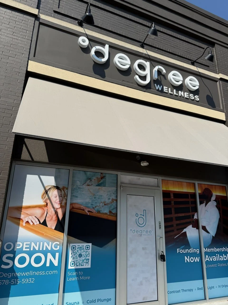 Storefront window advertising the opening of a wellness center called '0 degree wellness,' featuring images of people relaxing in a hot tub and receiving spa treatments, with signs indicating the opening is soon and memberships are available.