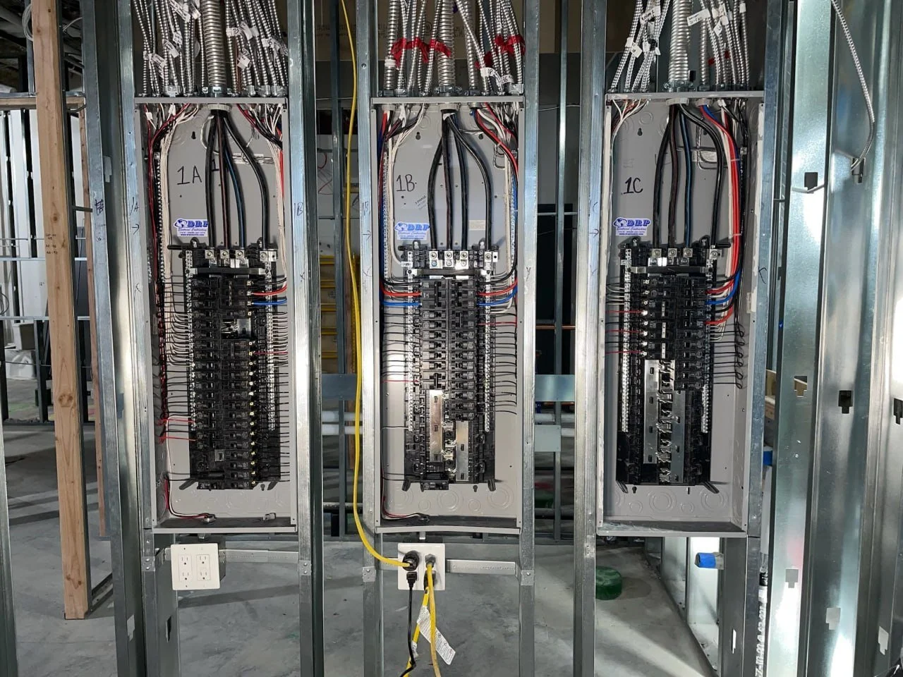 Electrical panels with wiring mounted inside a metal frame, with circuit breakers and connectors, in an unfinished building.