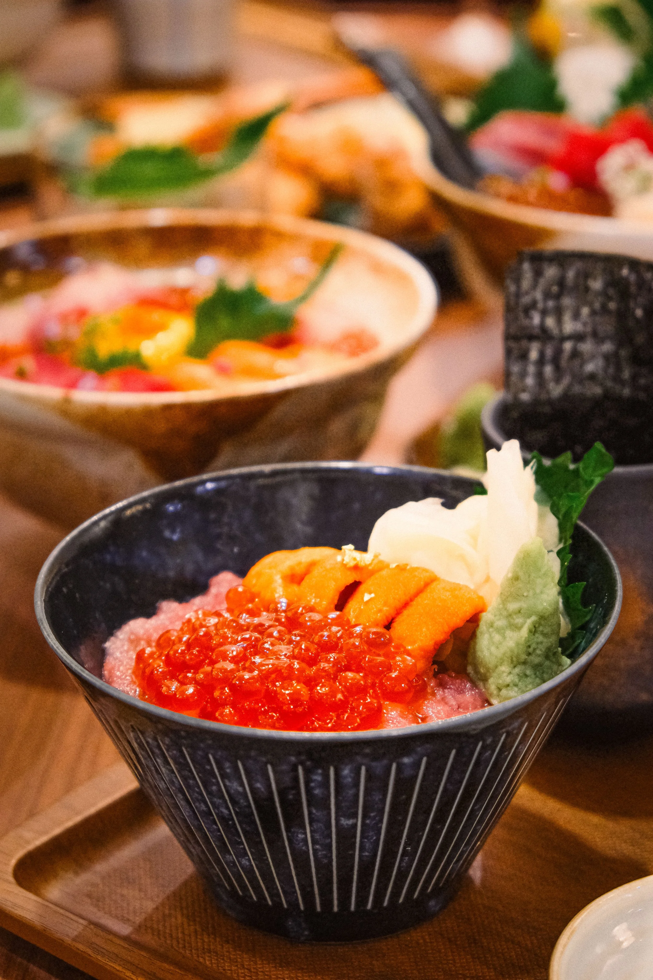 Bowl of sushi with salmon roe, sea urchin, and wasabi, served in a black bowl on a wooden tray.