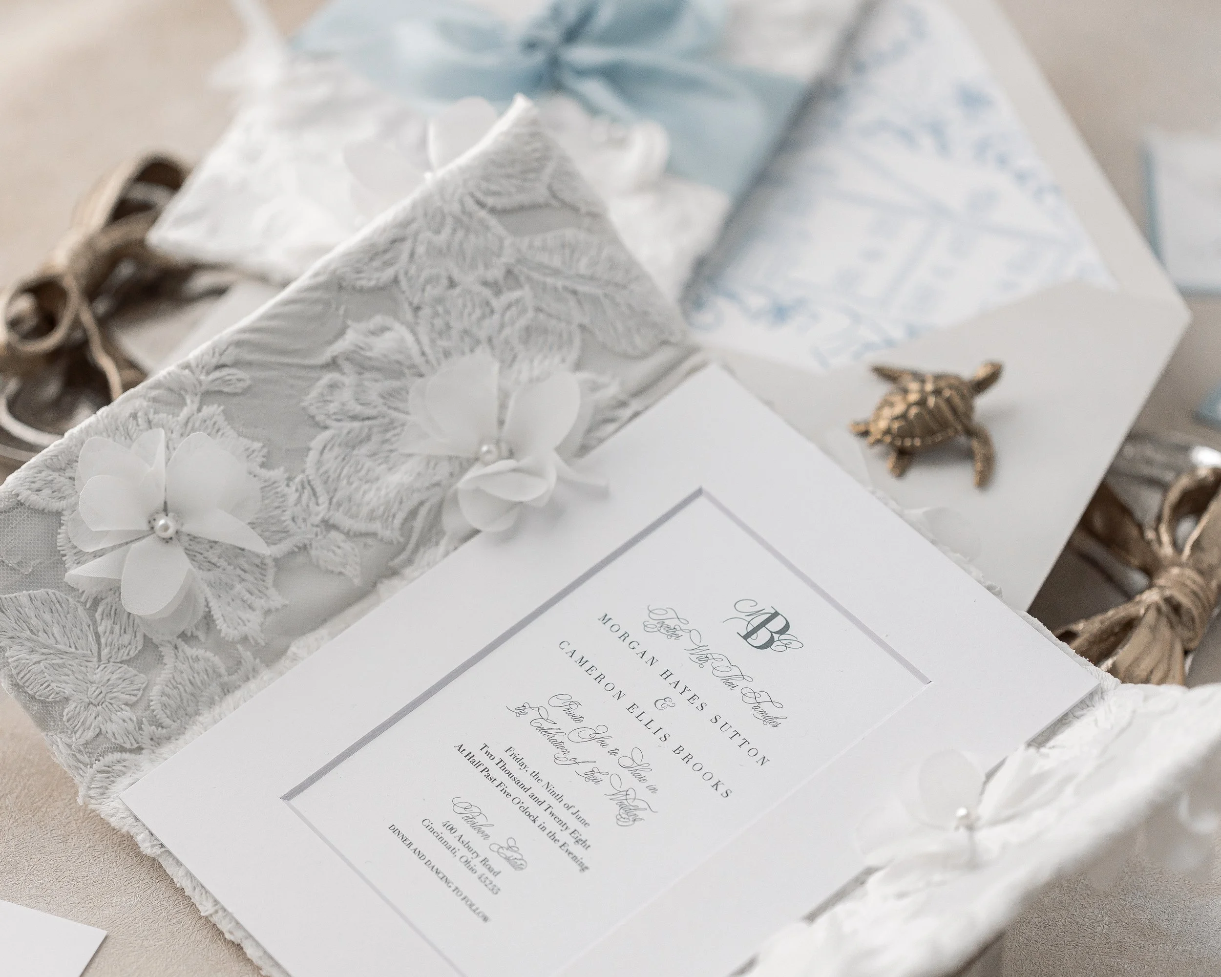 The gatefold unfolds to reveal textured fabrics, three-dimensional floral appliqués, and pearl embellishments that catch the light, inviting the touch and lingering admiration.