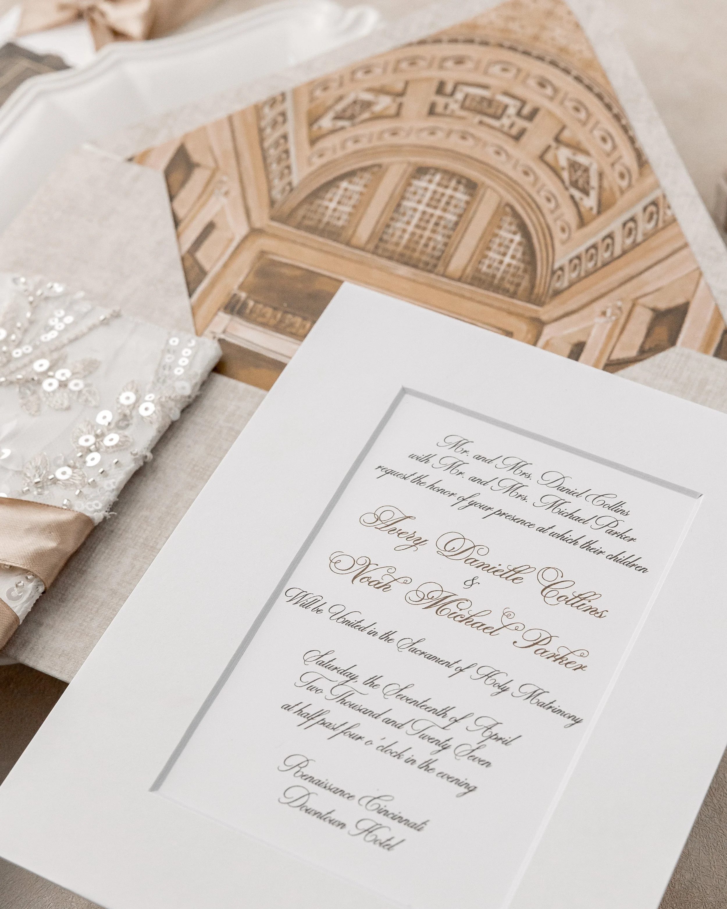 A full composition showcasing the dimensional matte-style invitation suite, hand-embellished fabric with sequins, champagne-gold embroidery, and gold satin ribbon, layered alongside coordinating envelope and guest details.