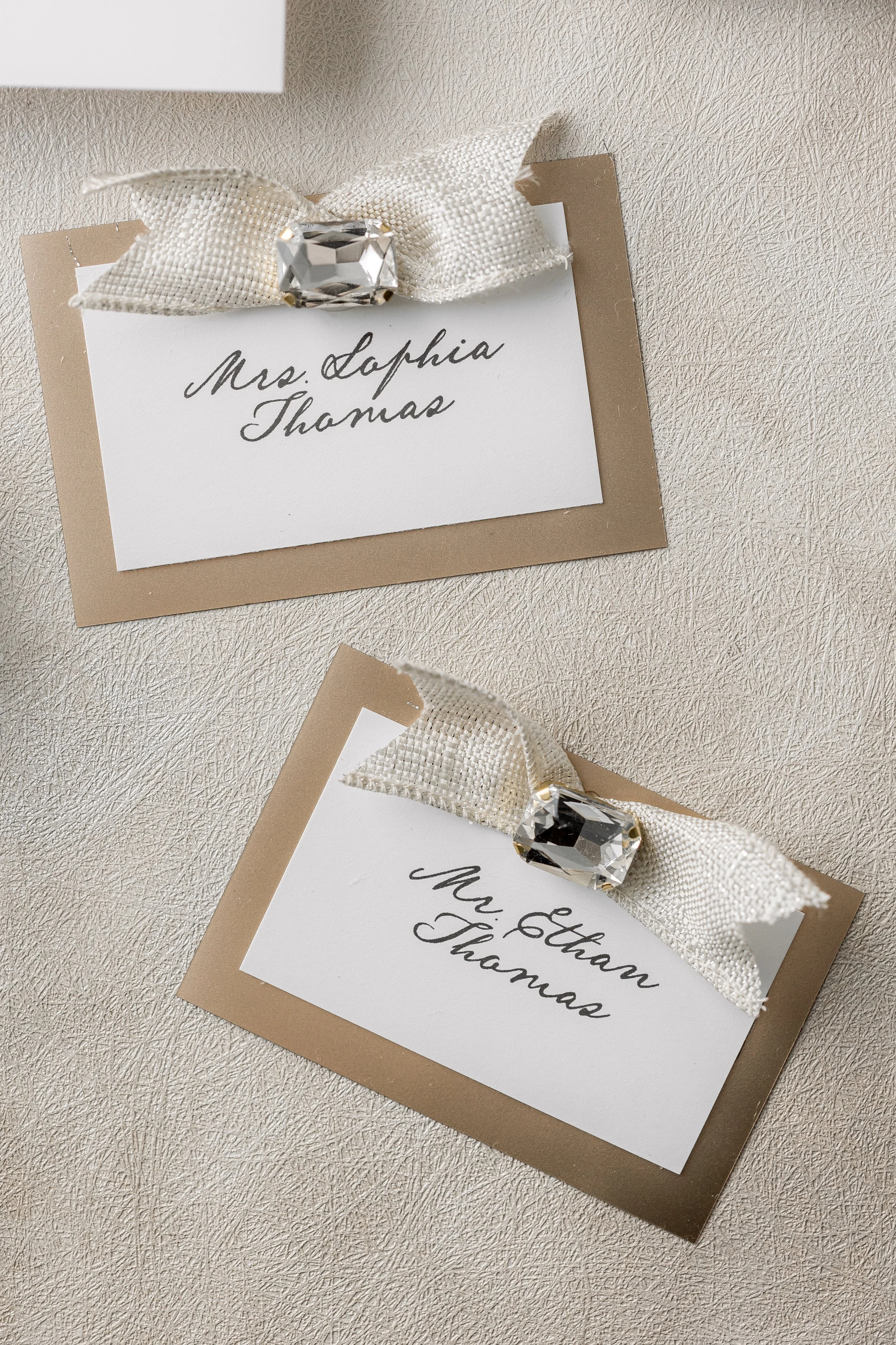 Each card is finished with matching gold-and-ivory foil ribbon, emerald-cut glass stones set in gold metal, and miniature metallic matting, ensuring a seamless connection to the main suite.