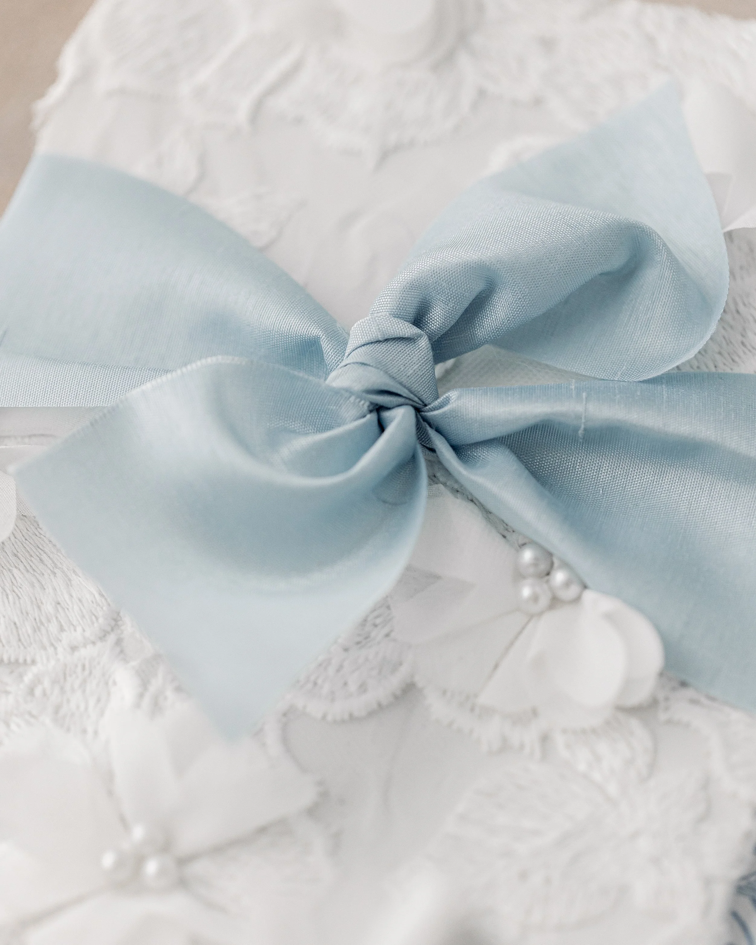 The two-inch dusty blue matte ribbon is tied with precision over the center, holding the gatefold structure together while adding a sculptural, refined accent.