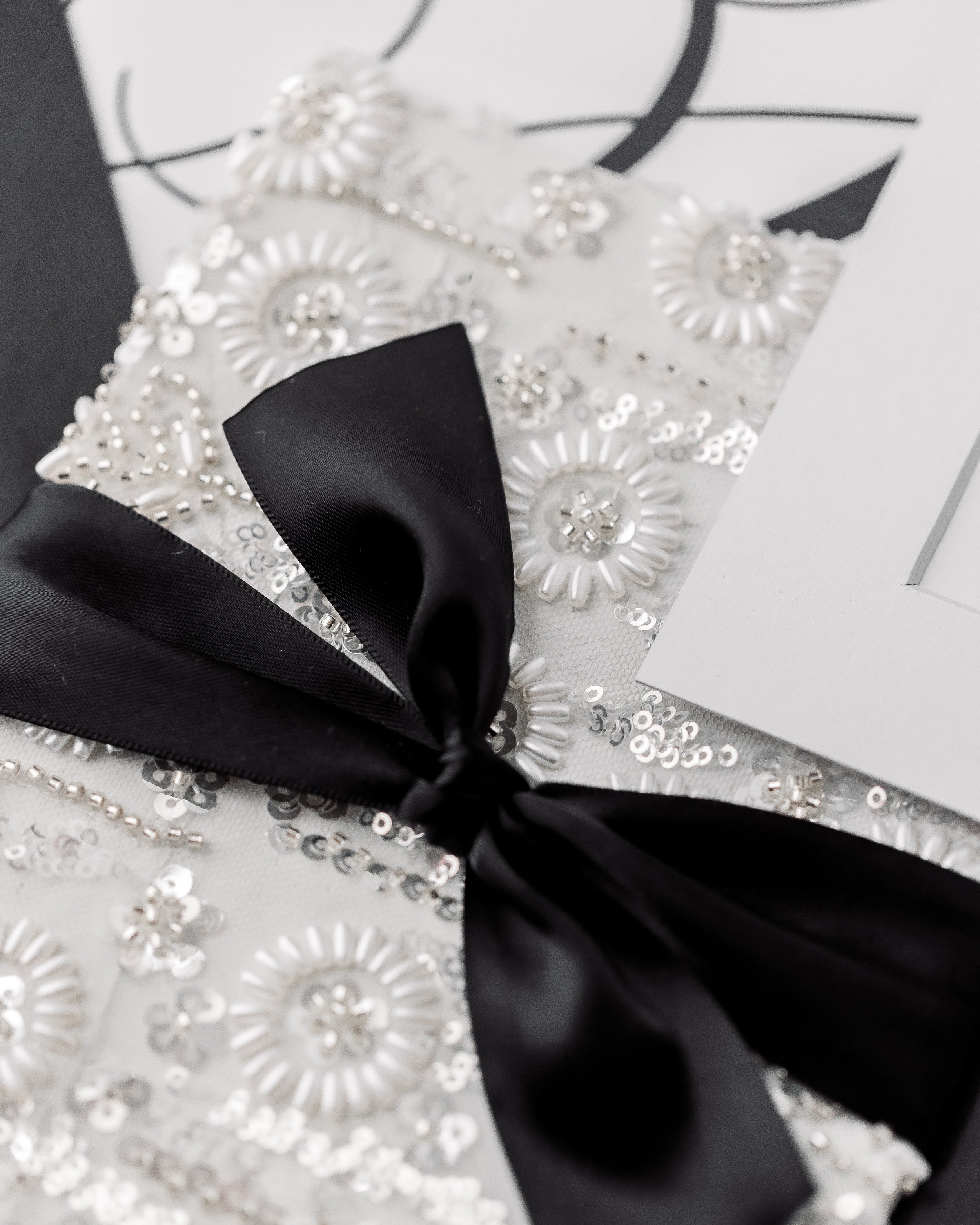 A black satin ribbon knot ties the layers together, its smooth sheen and sculptural fold harmonizing with the matte stock beneath.