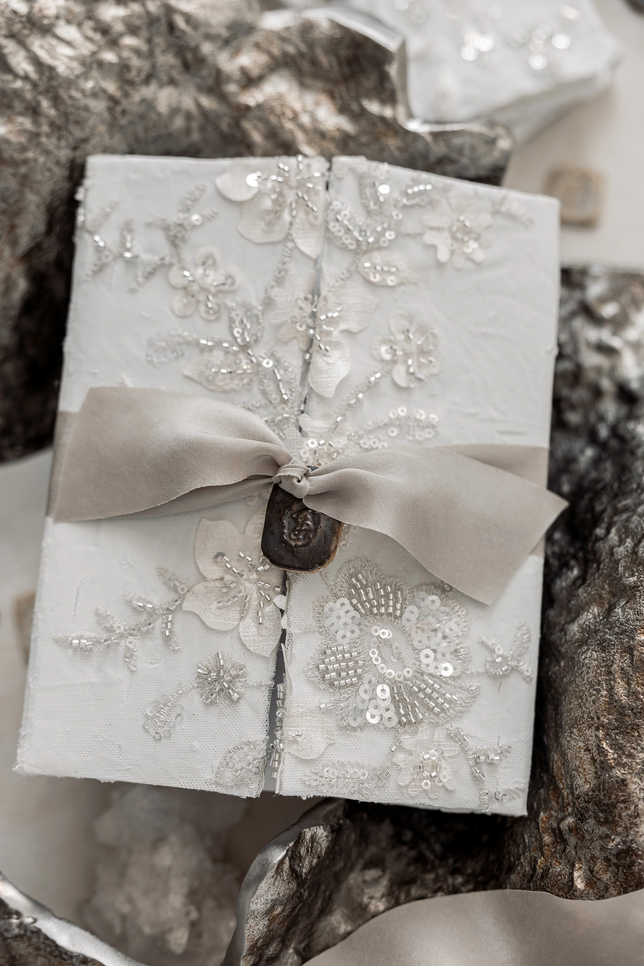 A custom cermaic charm stamped with a personalized monogram to match the interior of the gatefold, tied on with a hand-dyed silk ribbon.
