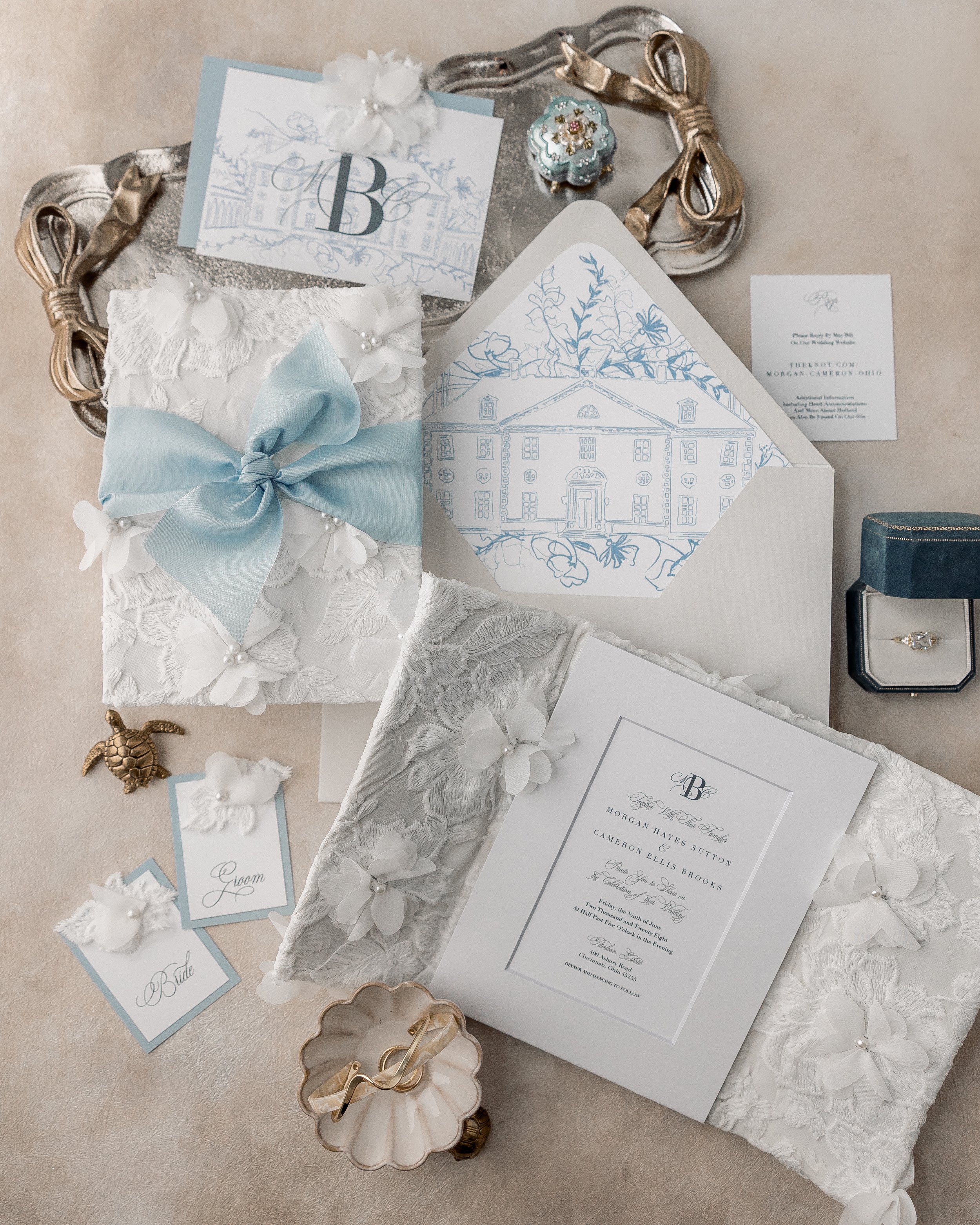 A full composition of the gatefold suite, showing the layered inner and back gates, textured fabrics, sewn pearl accents, and dust-blue matte ribbon tying the suite together.