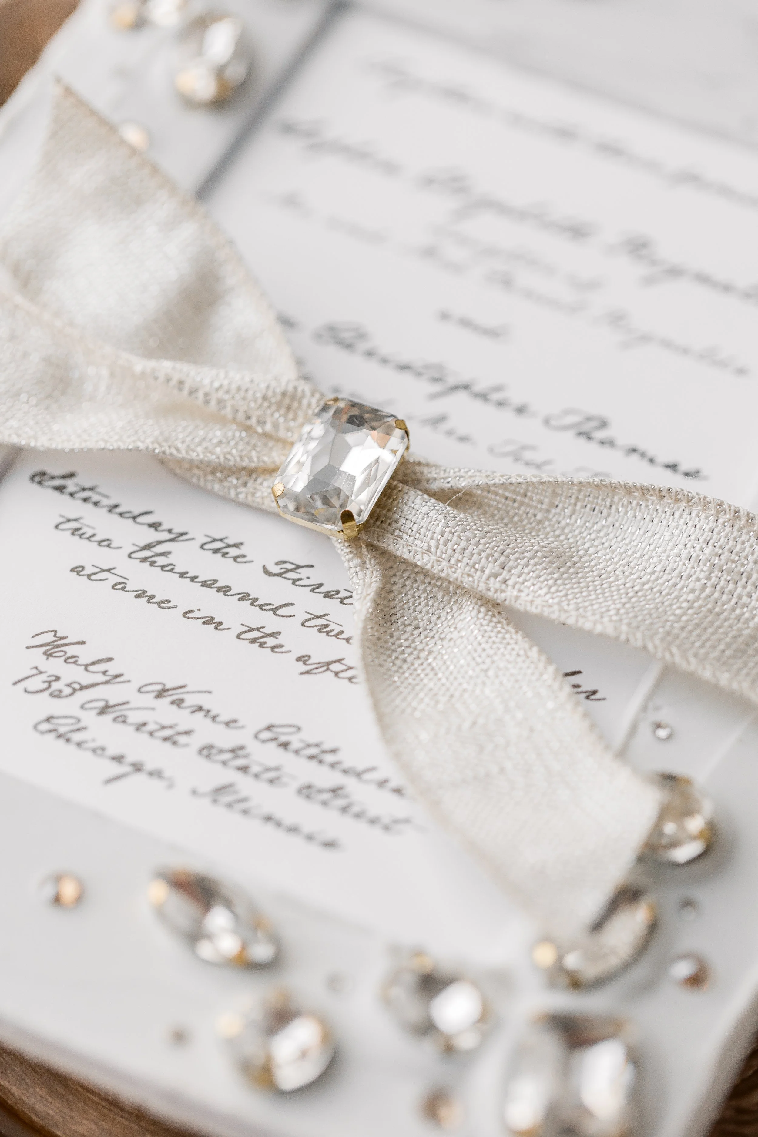 A close-up of the ribbon showcases the foil-threaded ivory tie, elegantly binding the suite while adding a reflective, tactile accent.