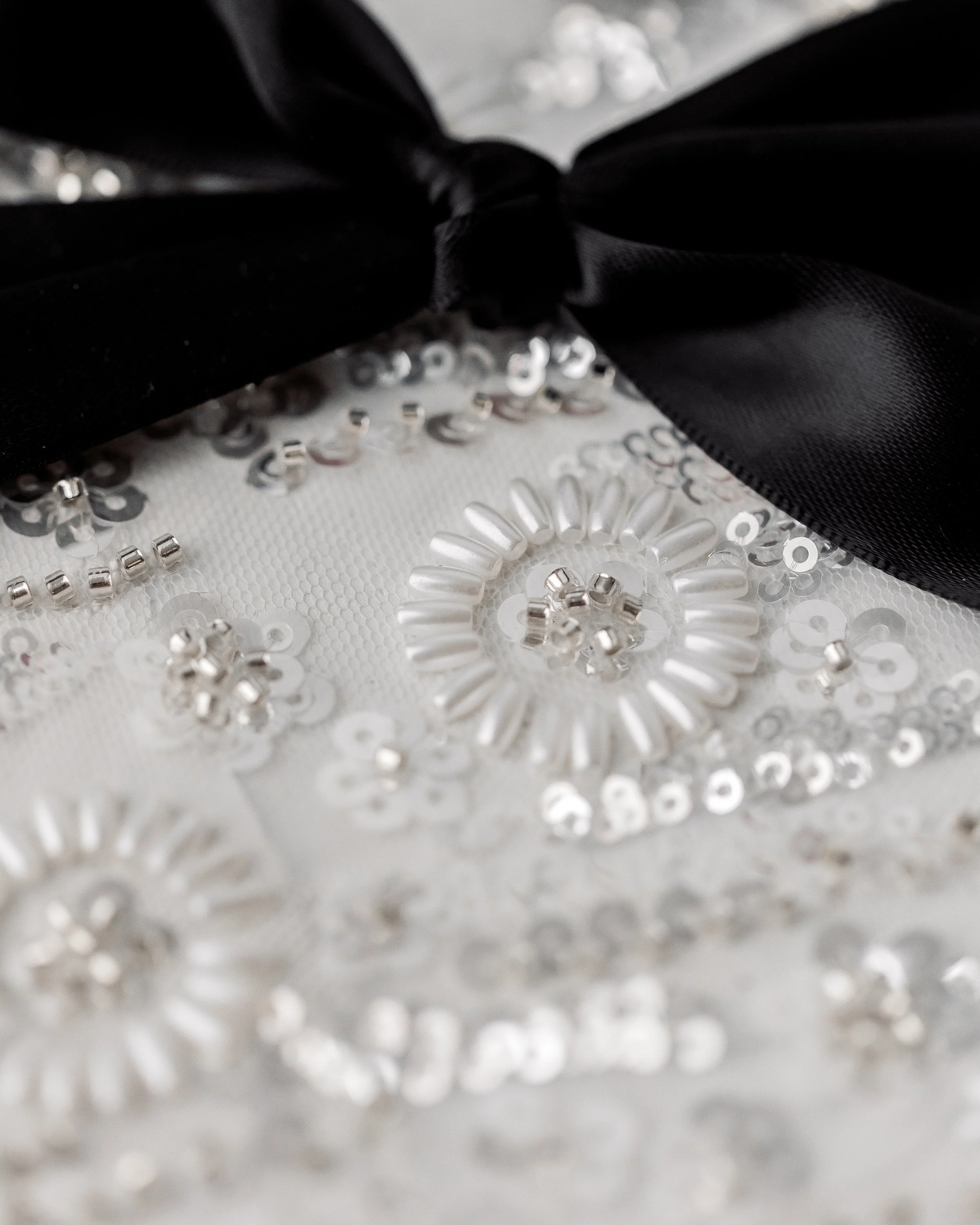 Light dances across the textured fabric on the back, where beads, sequins, and metallic threads rise like sculptural whispers against the matte base.