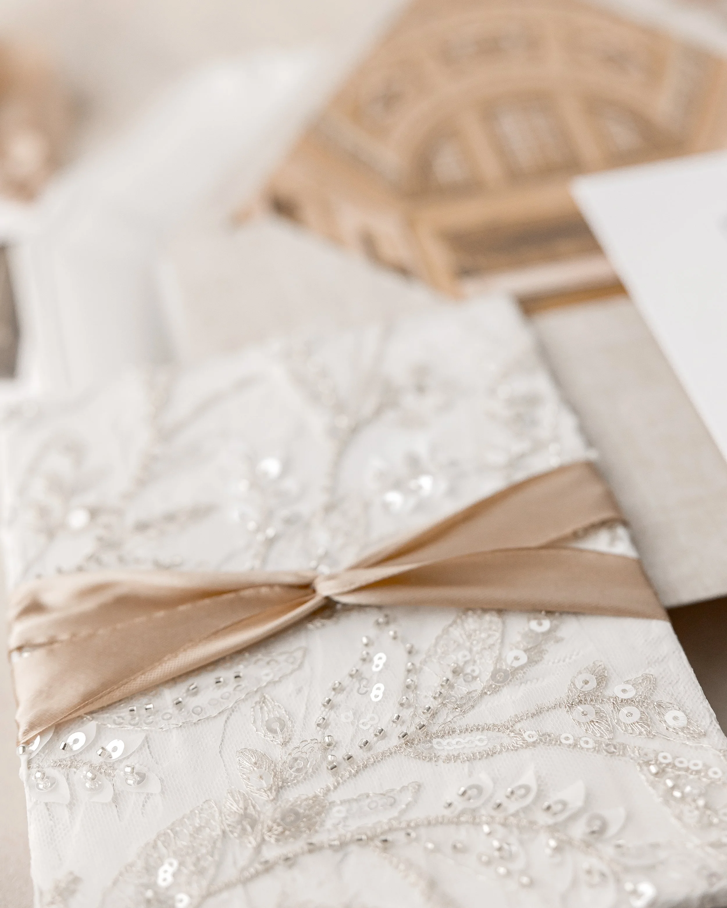 Flipping the invitation reveals hand-applied fabric leaves, sequins, and embroidery, secured with a gold satin ribbon twist tie, creating a tactile, dimensional experience.